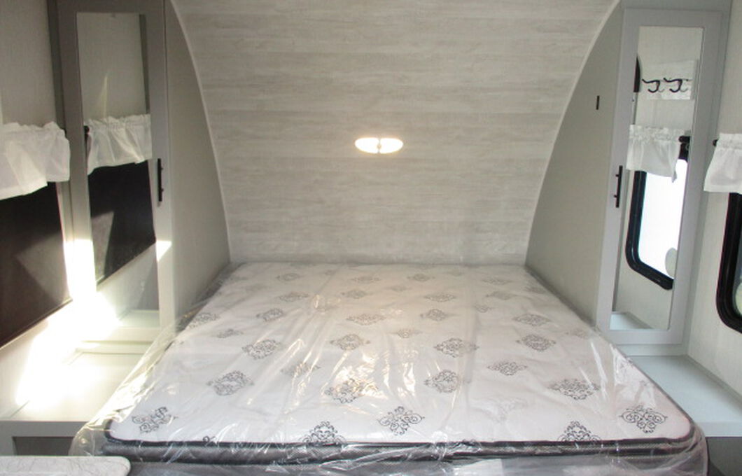 RV rental interior showing a compact bedroom with a new mattress, built-in storage, and mirror for convenient travel.. Forest River Vibe 2022