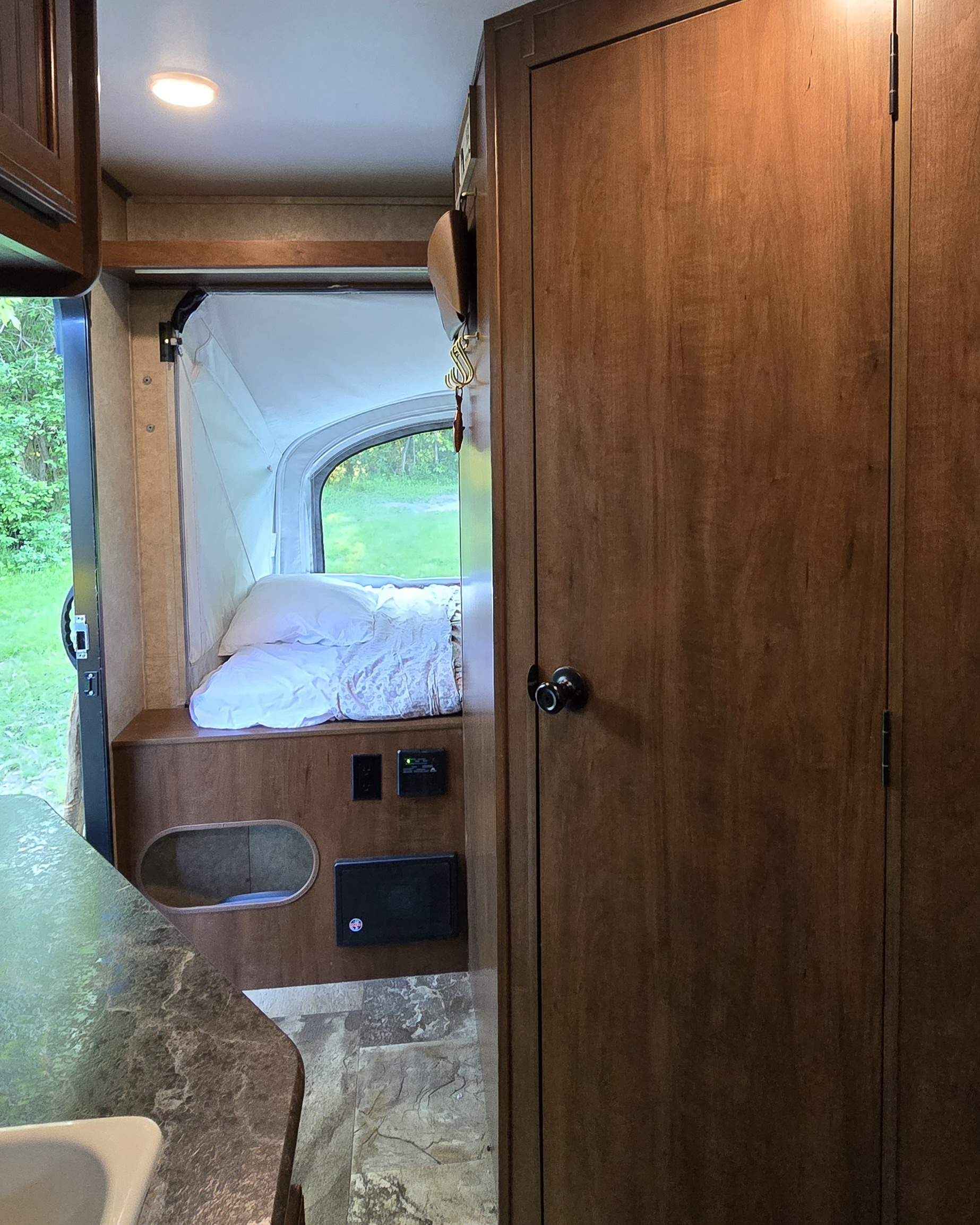 This RV rental interior features a comfortable sleeping bunk, a window with a serene forest view, and warm wood cabinetry.. Jayco Jay Feather 7 XRB 2016