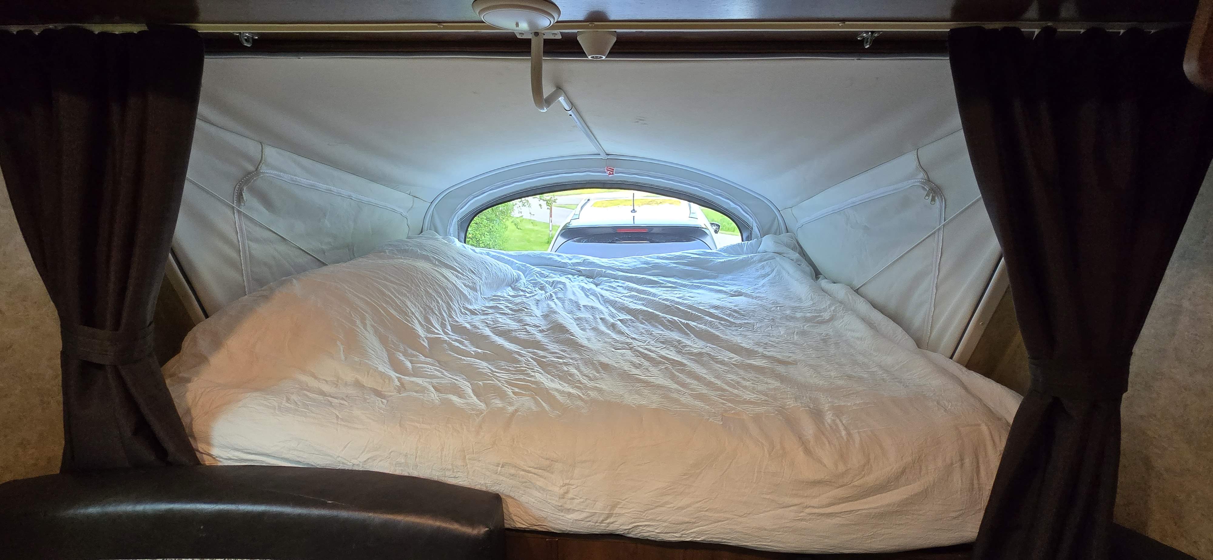 Cozy RV rental interior: large bed, tied-back curtains, and window view looking out of the pop-up camper.. Jayco Jay Feather 7 XRB 2016