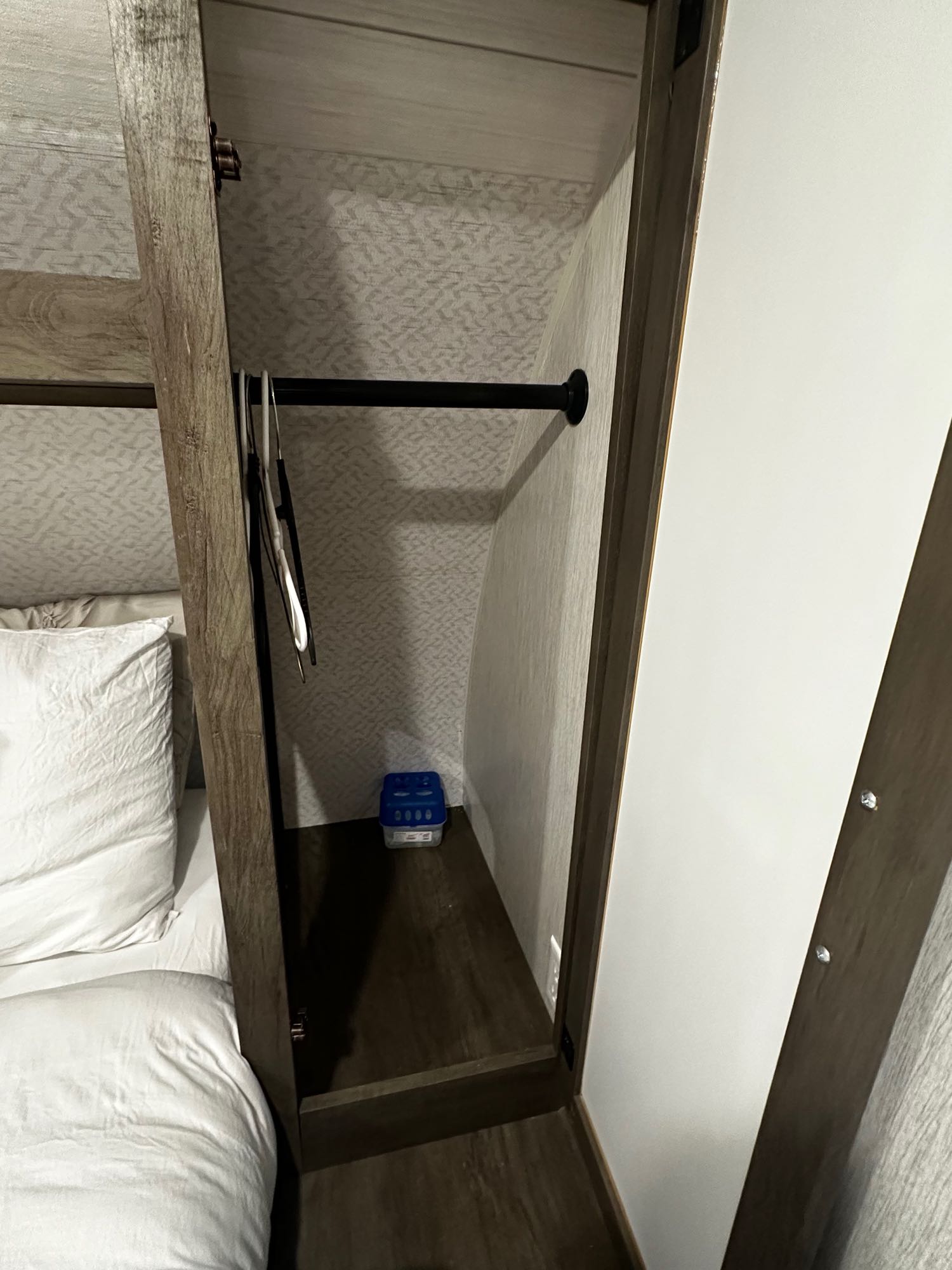 RV rental bedroom: compact closet with hanging rod, hangers, and a small blue box. A comfy bed is visible left.. Forest River Salem Cruise Lite 2022