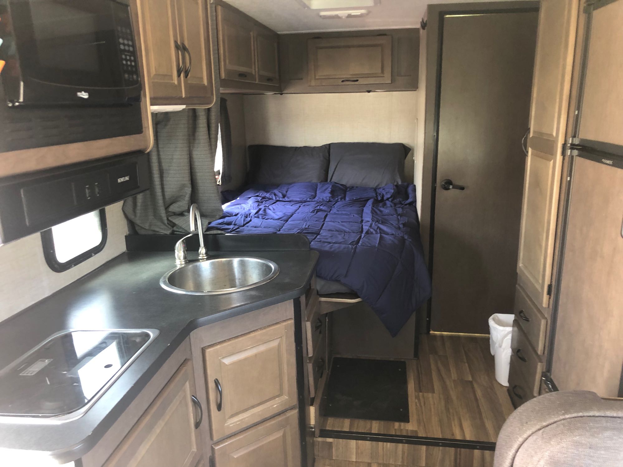 Compact RV rental interior: kitchenette with sink and stove on left, bed with blue comforter on right.. Thor Majestic 2018