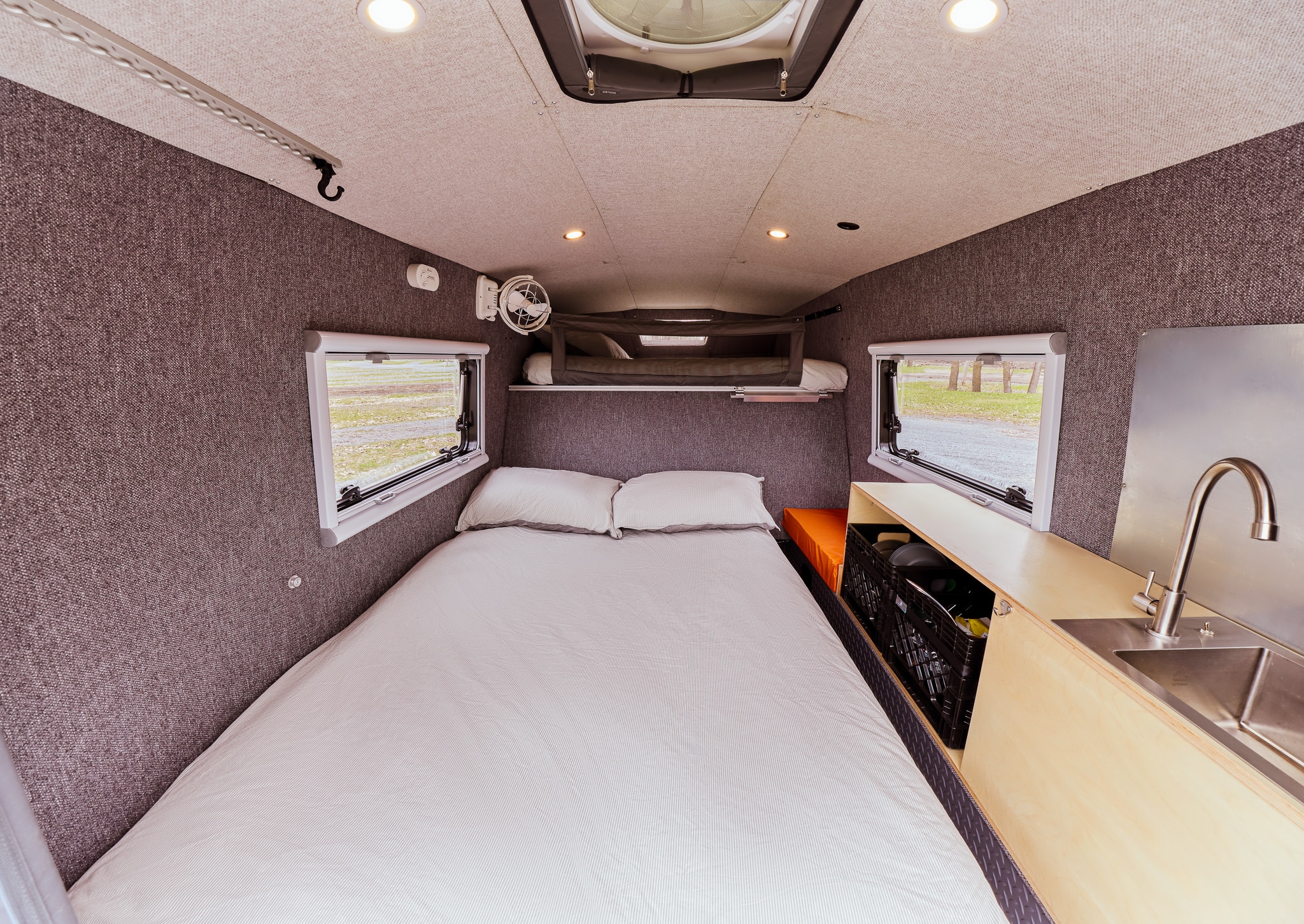 RV rental interior featuring a large bed, compact kitchen with sink, and overhead bunk. Ideal for camper adventures.. Gmc sierra 1500 2024