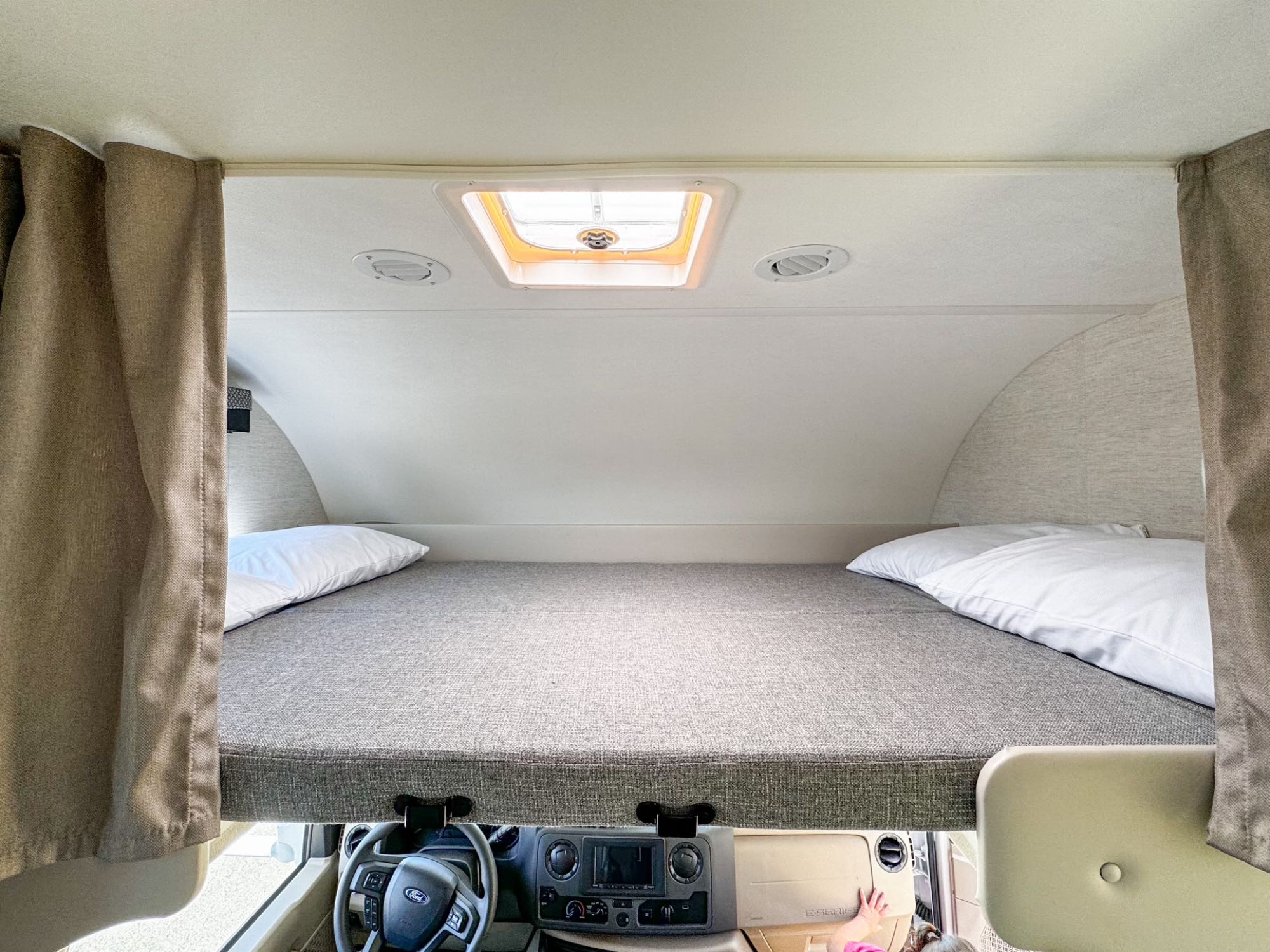 Cozy cab-over bunk bed in an rv rental, featuring a skylight, air vents, and privacy curtains for comfortable sleeping.. Thor Freedom Elite 2024