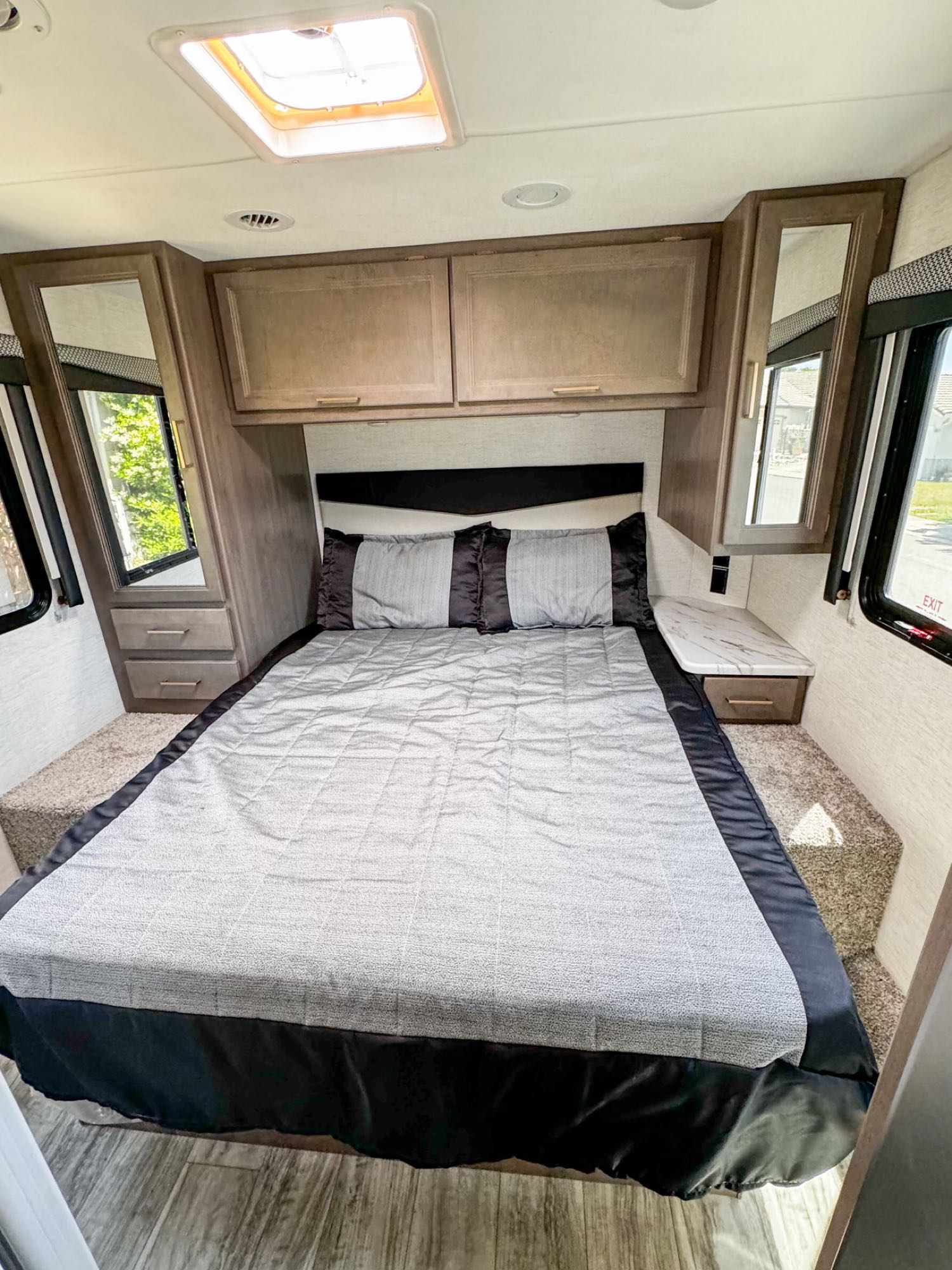 RV rental bedroom featuring a comfy bed, overhead storage, mirrored side cabinets, and bright windows.. Thor Freedom Elite 2024