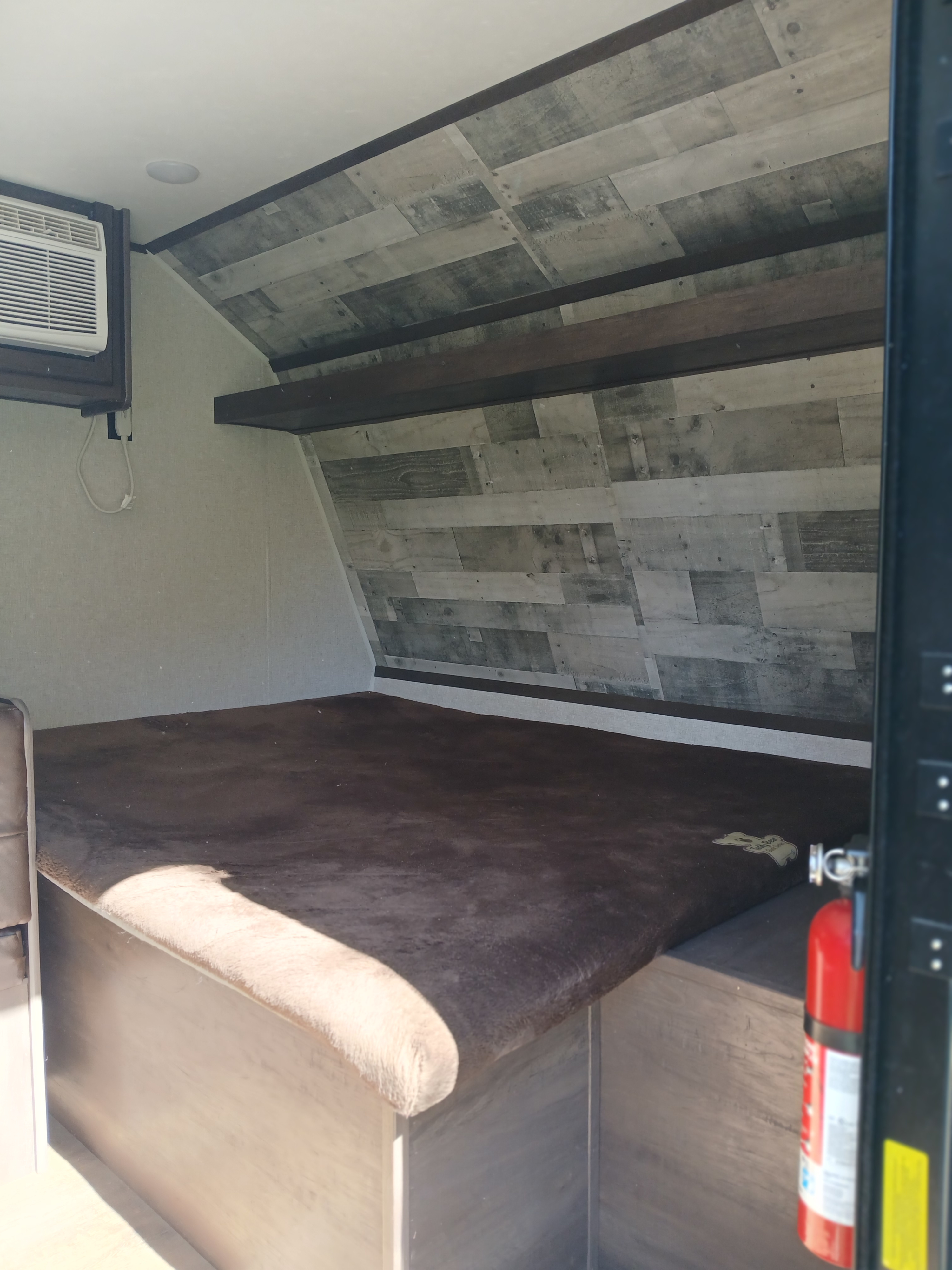 RV rental bedroom features a comfortable dark bed, AC unit, and unique wood-paneled walls. Fire extinguisher visible.. Coleman Lantern 2021