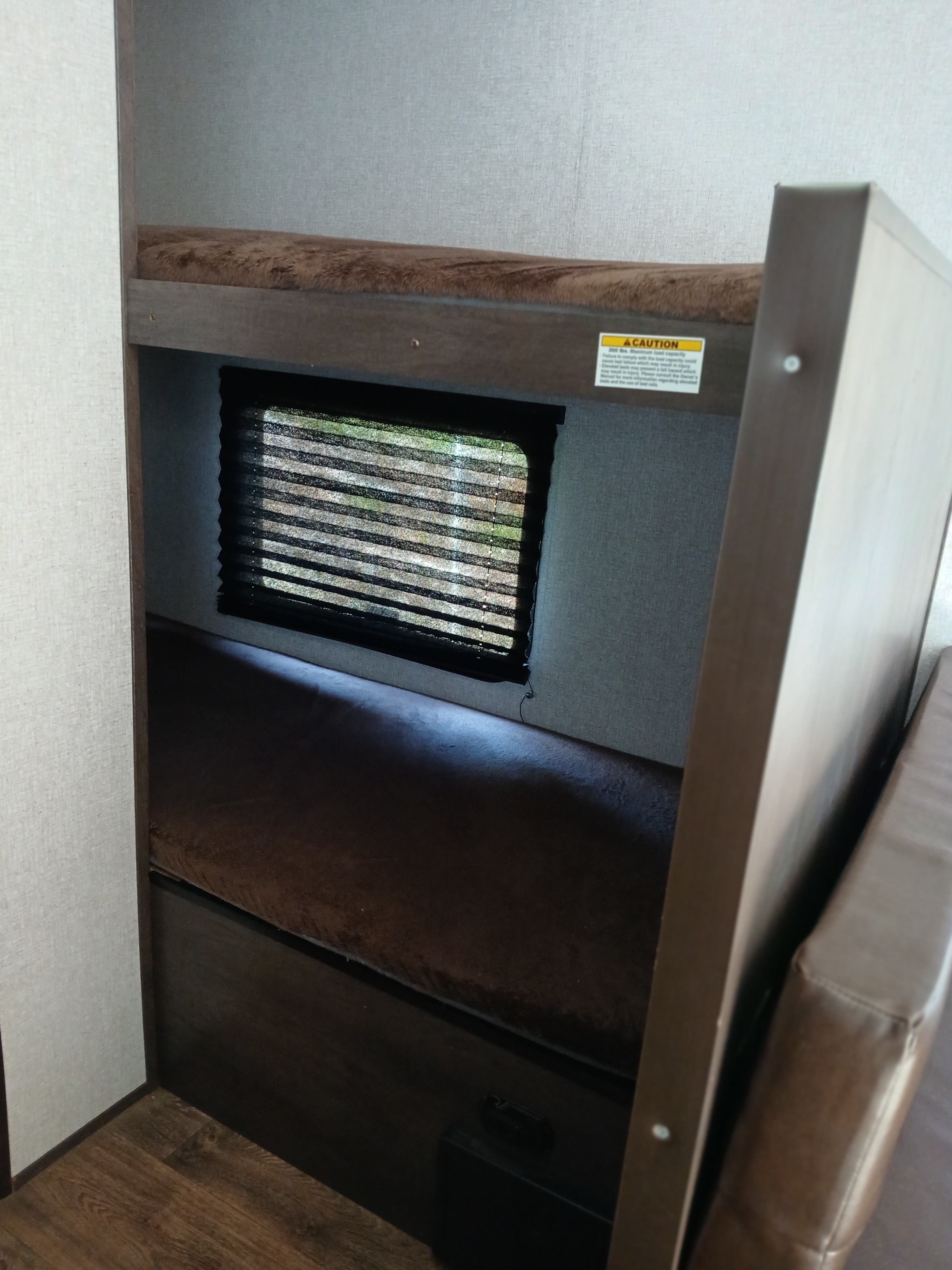 Inside an RV rental: two brown bunk beds with a window and blinds. Top bunk has a safety warning label.. Coleman Lantern 2021