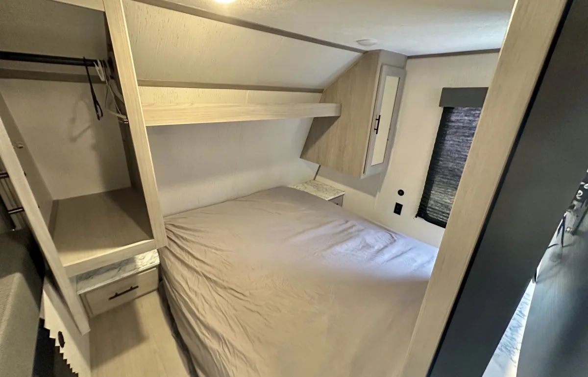 Inside an RV rental: a cozy bedroom featuring a neatly made bed, overhead shelf, closet, and window for comfortable travels.. Dutchmen Coleman Lantern 2022