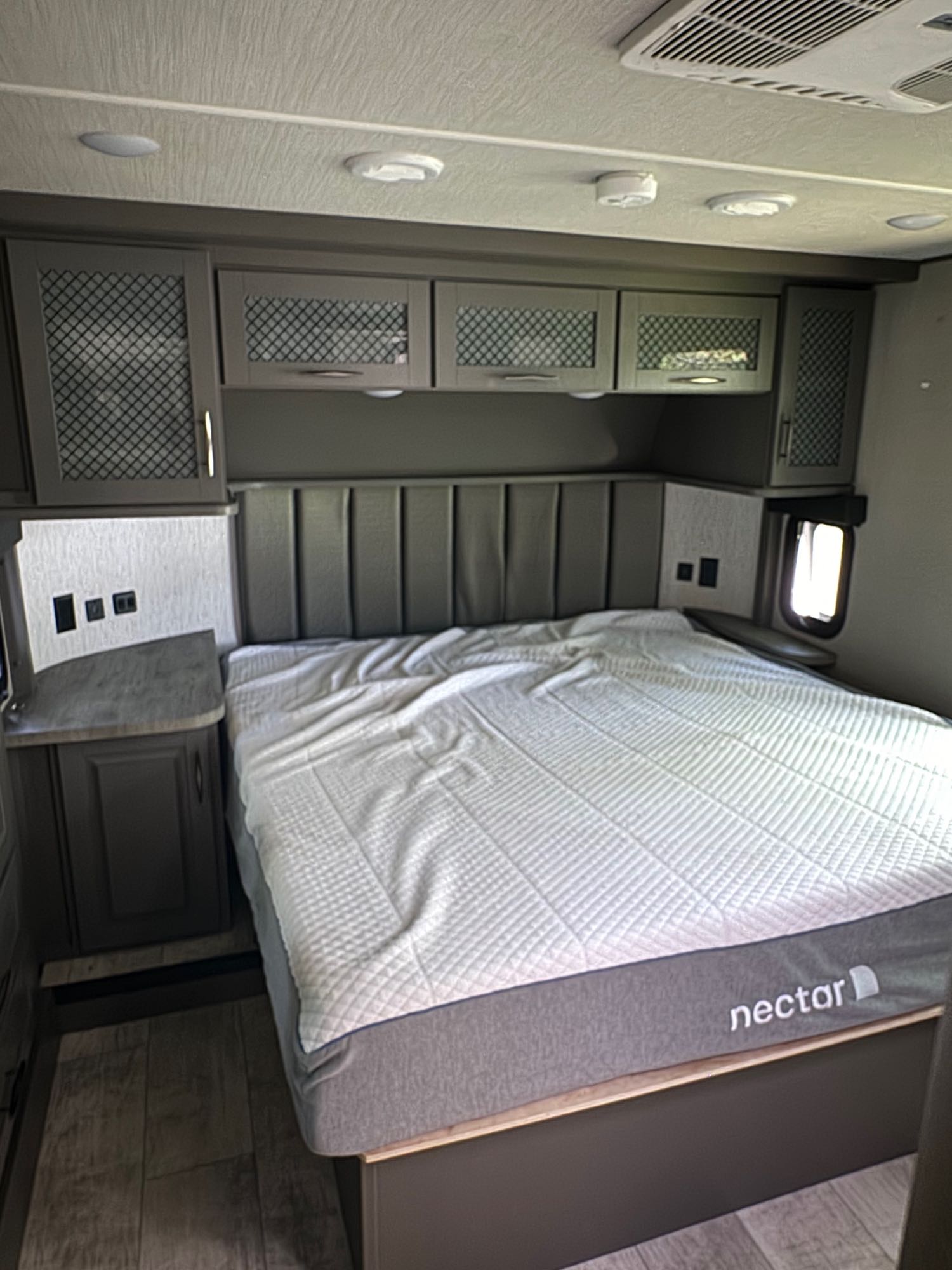 Comfortable RV rental bedroom featuring a Nectar mattress, padded headboard, and built-in storage cabinets.. Grand Design Momentum Toy Hauler 2022