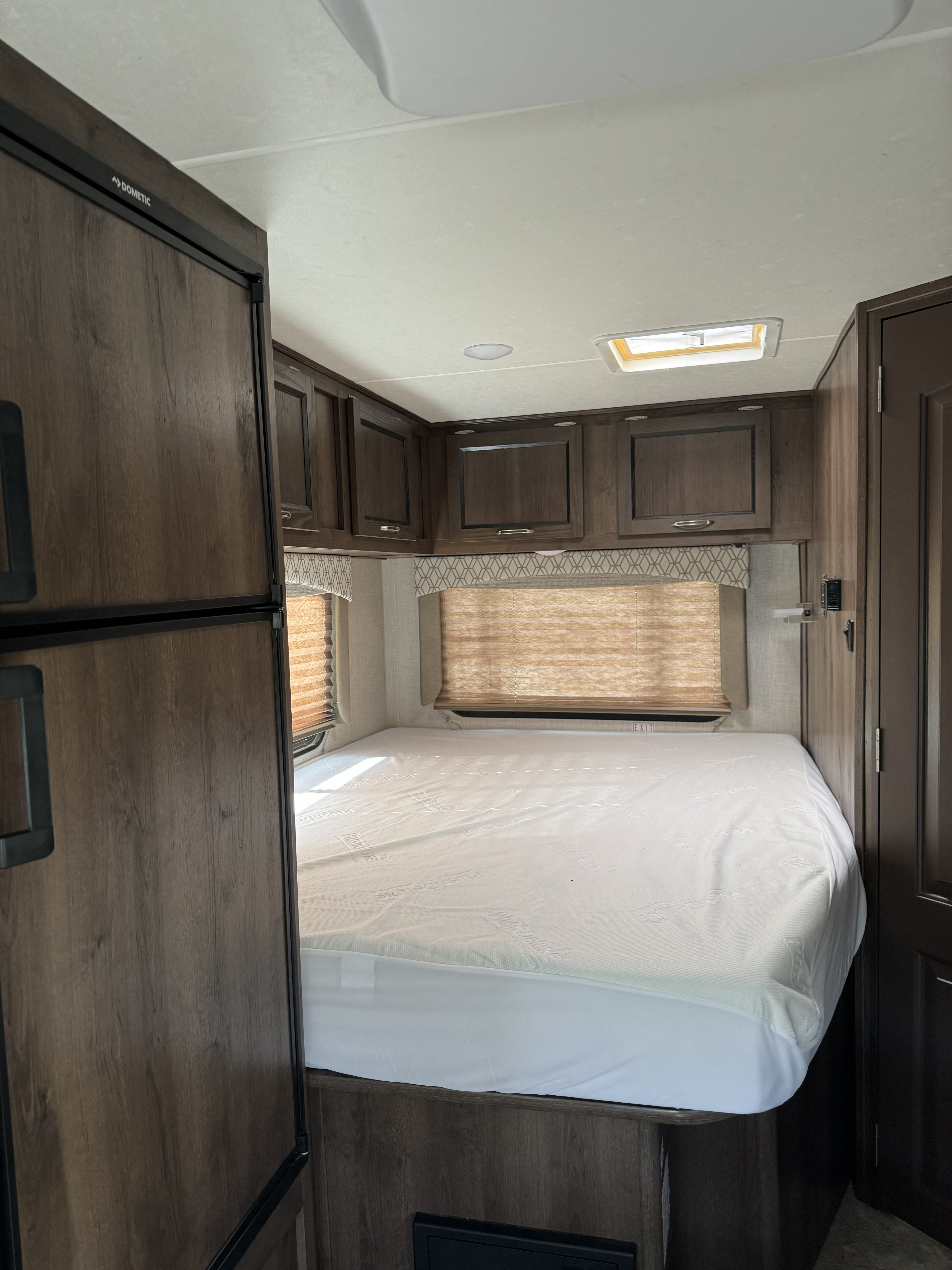 Spacious RV rental bedroom with a comfy bed, overhead cabinets, and natural light from windows and a skylight.. Forest River Coachmen Freelander 2020