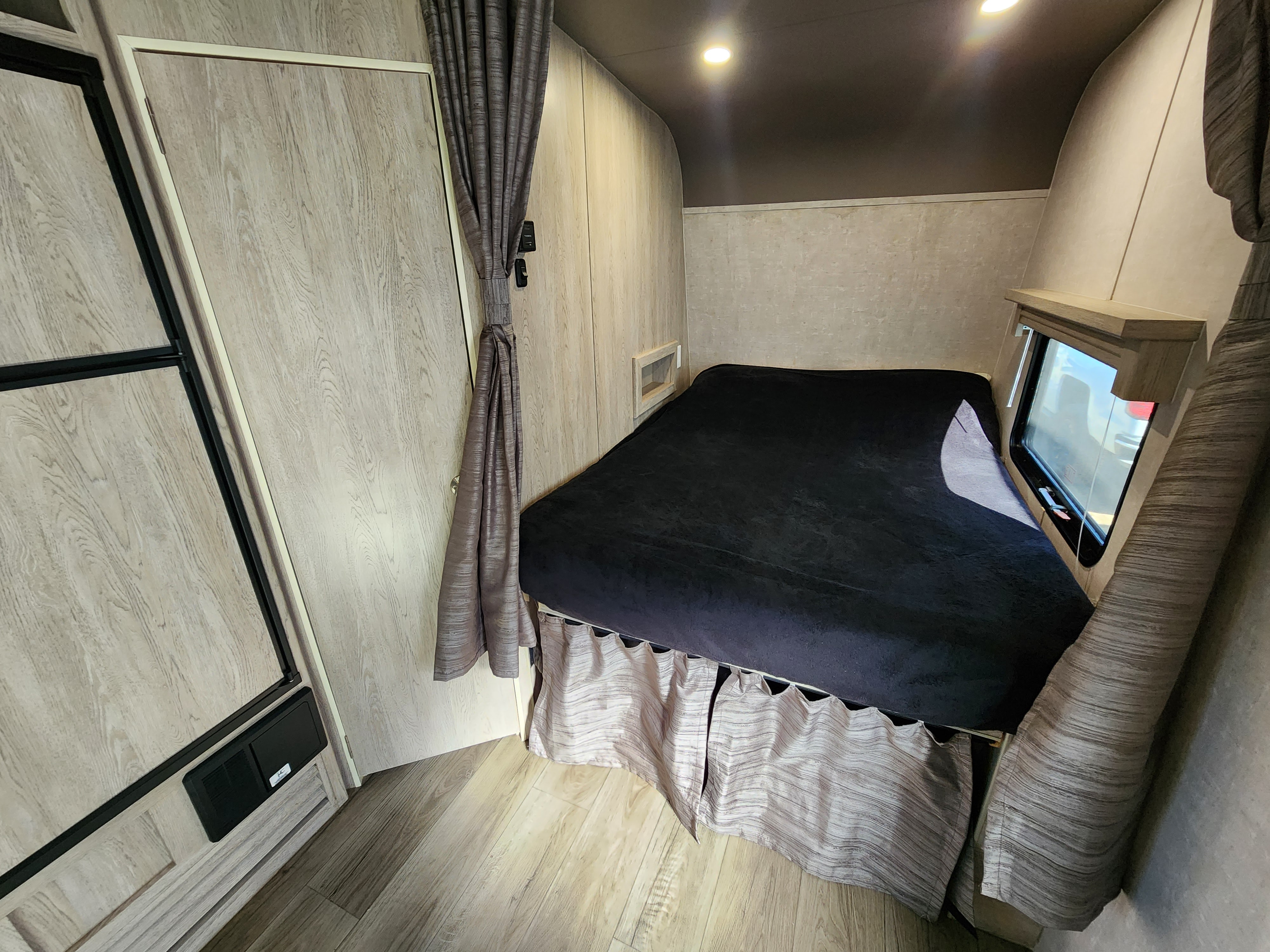 RV rental bedroom: a cozy retreat with a dark bed, light wood-look walls and storage, tied-back curtains, and a window.. Eclipse Recreational Vehicles Stellar 2021
