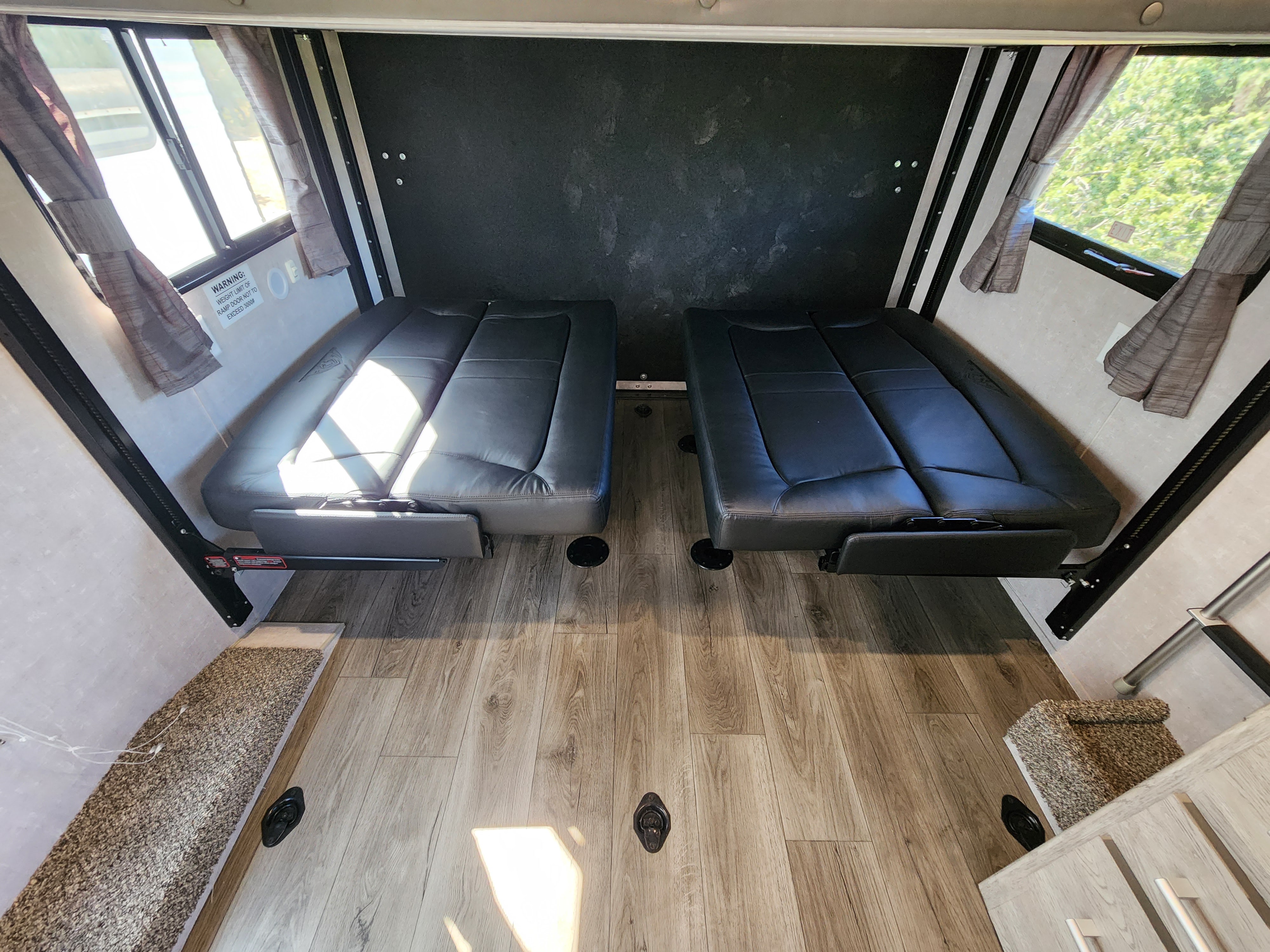 RV rental's versatile cargo/living space: two convertible benches, wood-look floor, and windows with curtains.. Eclipse Recreational Vehicles Stellar 2021