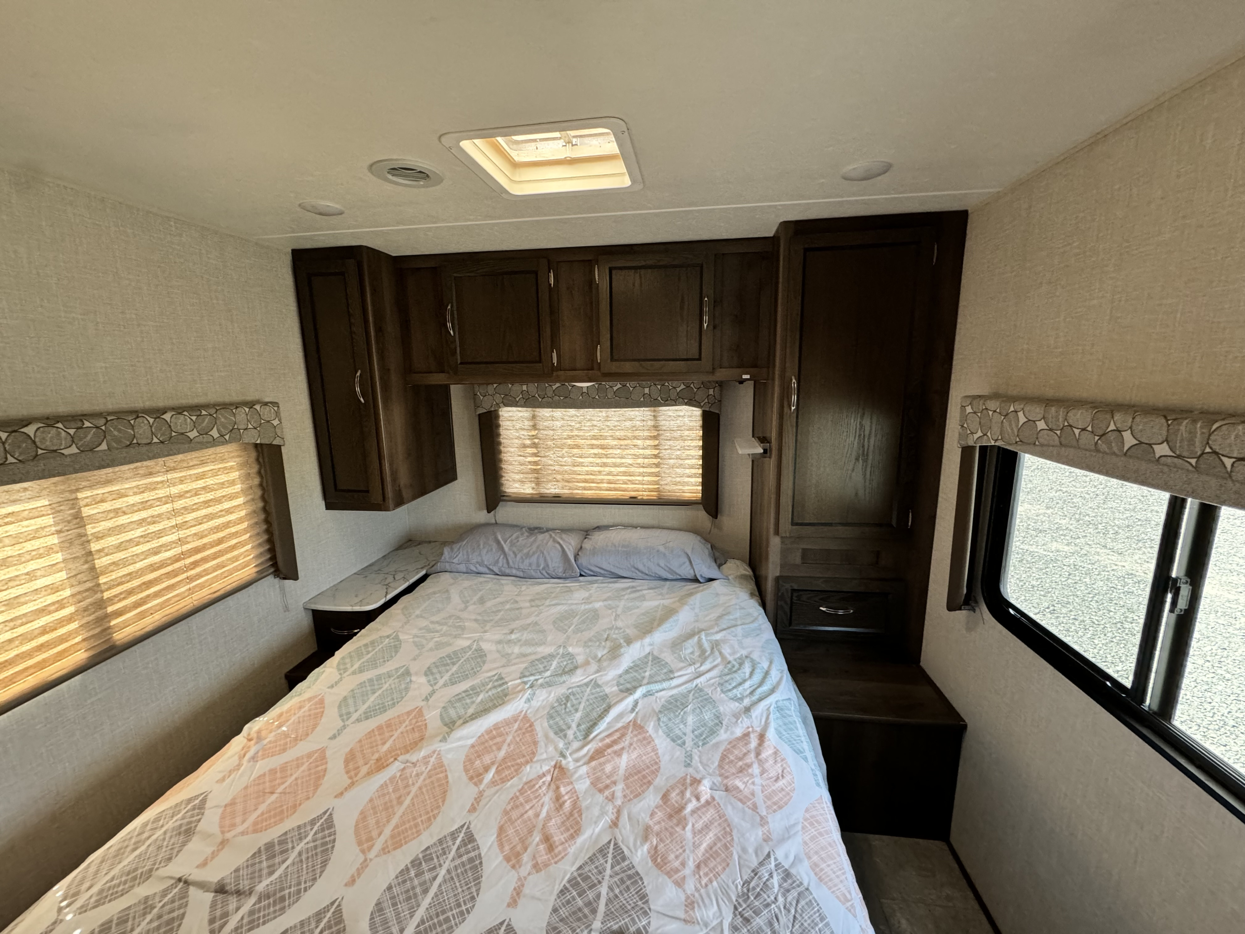 RV rental bedroom: a cozy space with a patterned bed, overhead cabinets, and windows for natural light.. Forest River Coachmen Freelander 2020