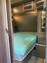 This RV rental's cozy bedroom features a comfy bed with a green topper, overhead cabinets, and a wardrobe. Great for travel!. Forest River Surveyor 2018