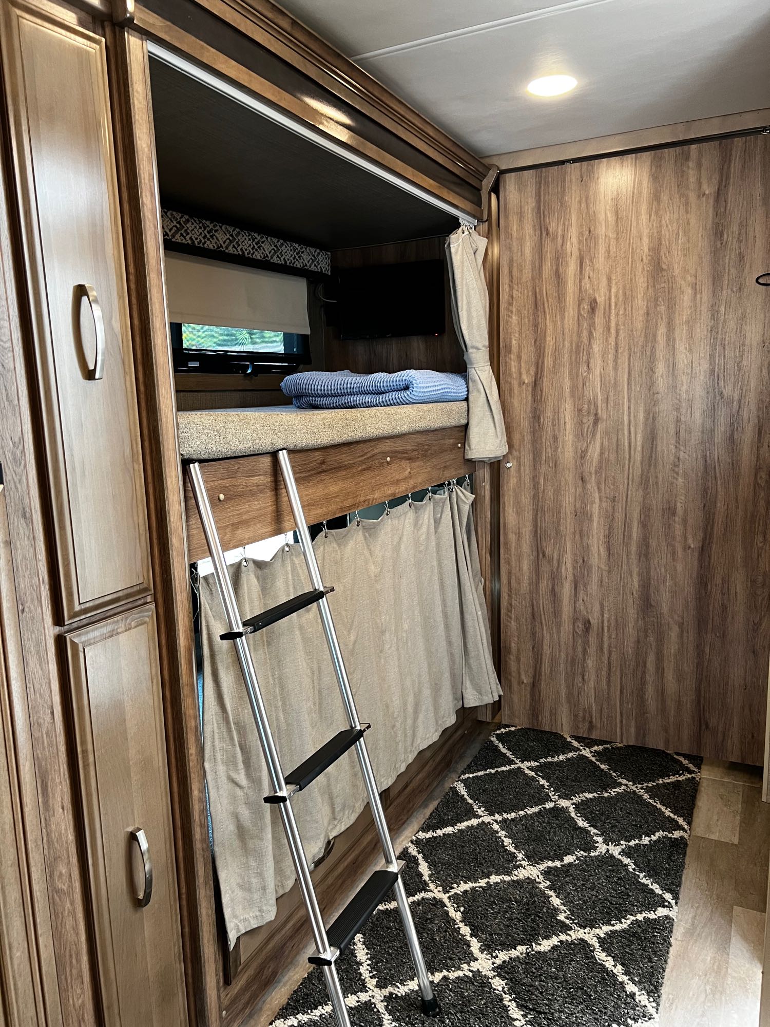 Cozy RV rental bunk beds with ladder, privacy curtain, and TV. Ideal for family travel, offering compact living space.. Jayco Seneca 2021