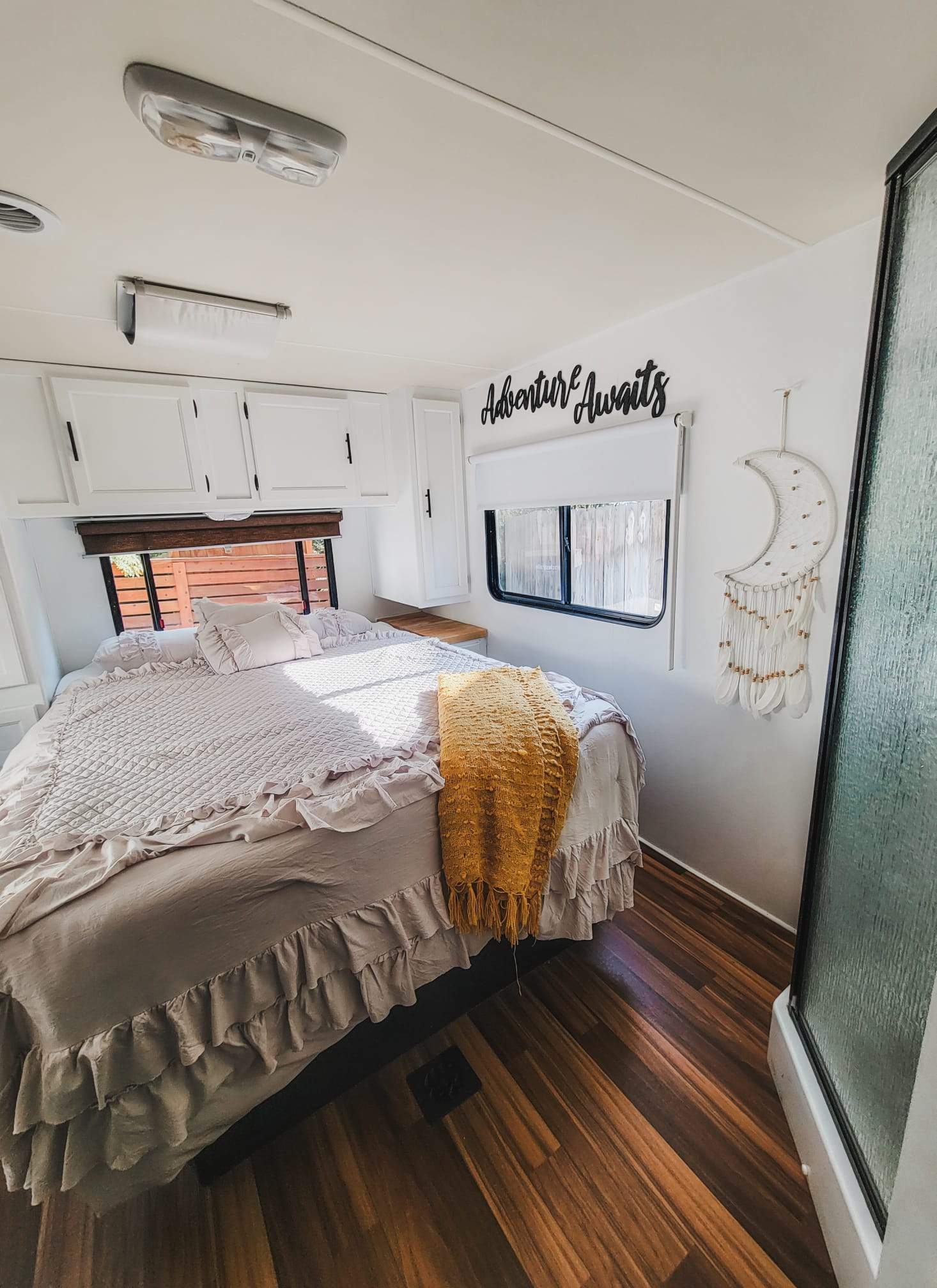 Cozy RV rental bedroom features a large bed with ruffle bedding, white cabinets, & 'Adventure Awaits' sign. Bright & inviting.. Coachmen Freelander 2014
