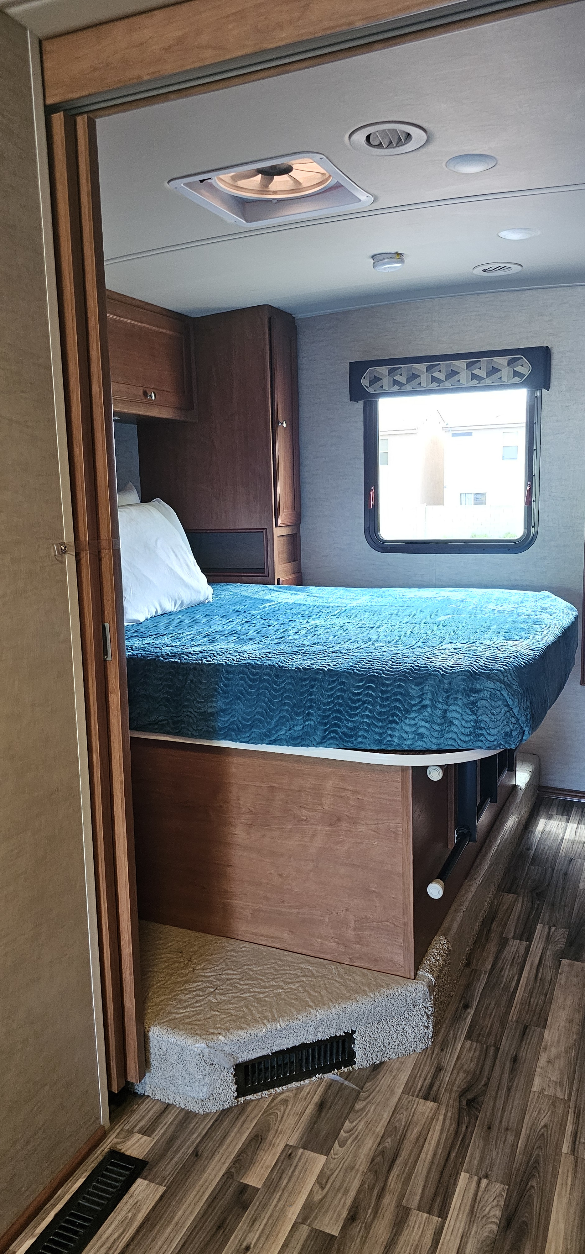 RV rental interior: cozy bedroom with a blue bed, wooden cabinets, window, ceiling fan, and floor vents.. Winnebago Vista 2017