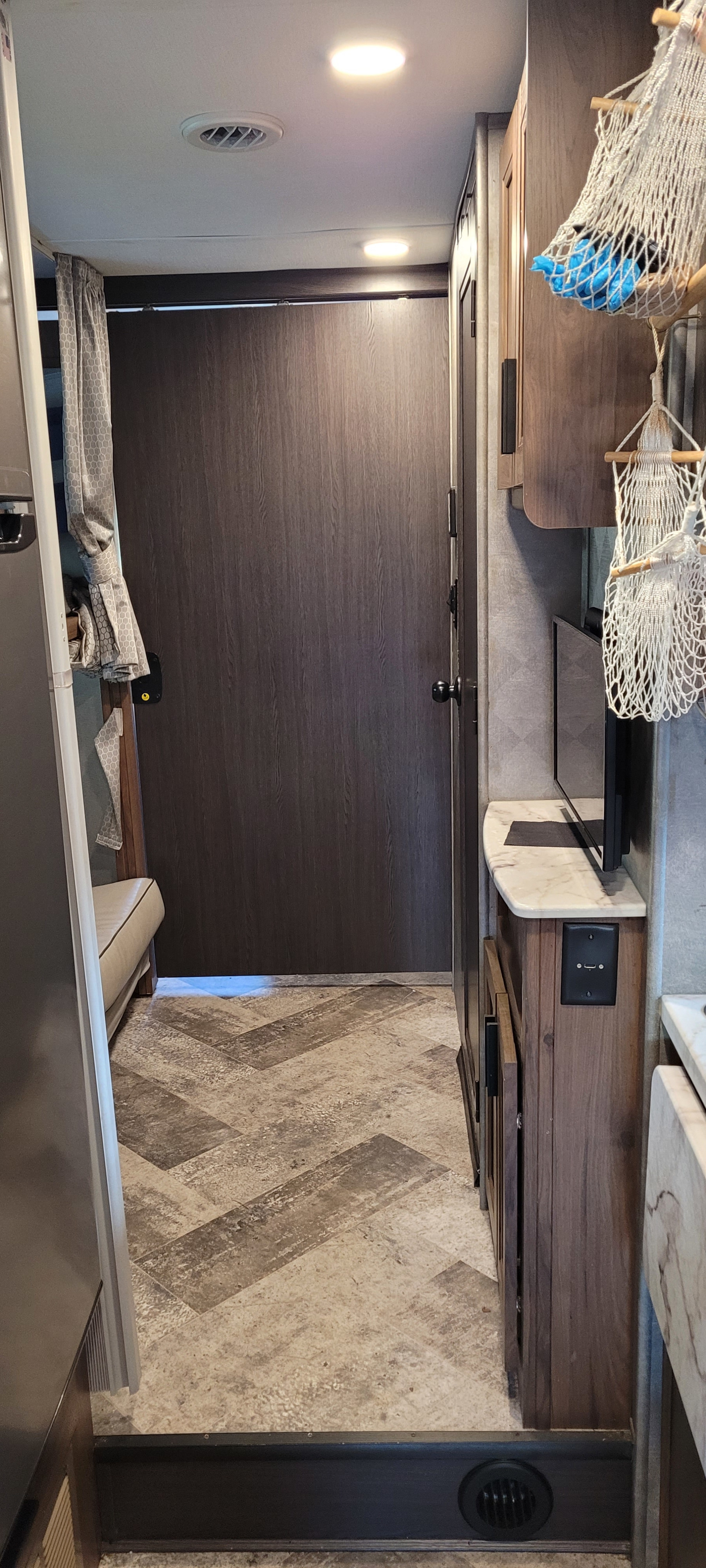 RV rental interior: a bright, narrow hallway with wood cabinets, a TV, patterned floor, and a glimpse of a bed/bunk.. Forest River Sunseeker LE 2020