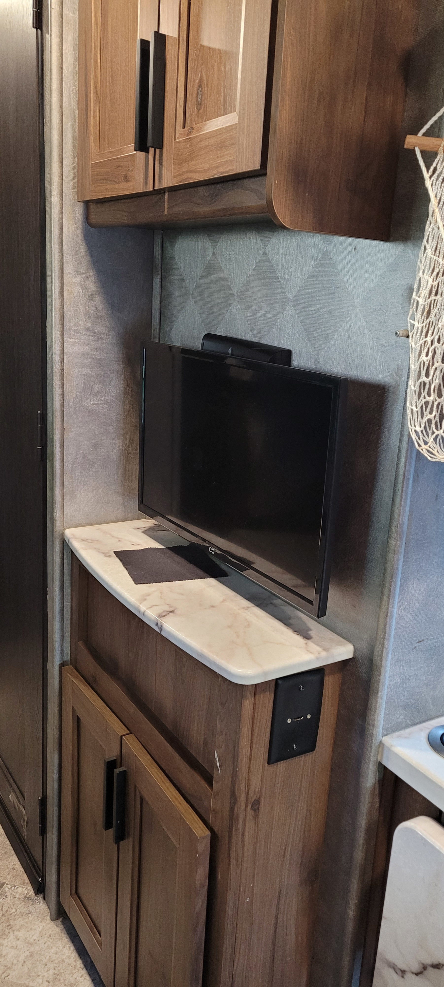 Cozy RV rental nook with wood cabinets, a TV on a light countertop, textured wall, and charging port.. Forest River Sunseeker LE 2020