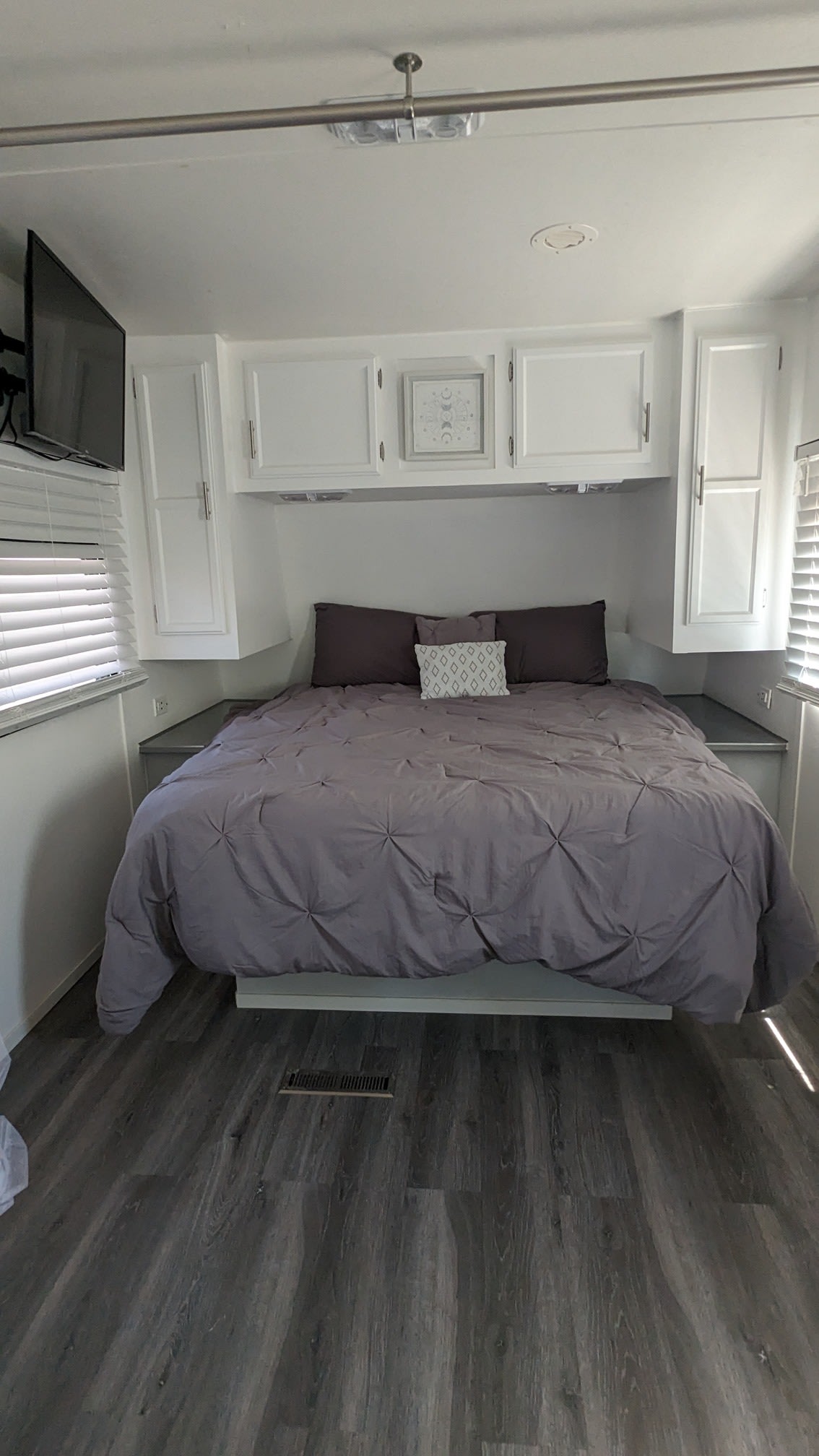 Modern RV rental bedroom featuring a large bed with gray bedding, overhead white cabinets, and a TV for comfortable stays.. Jayco Jay Flight 2011