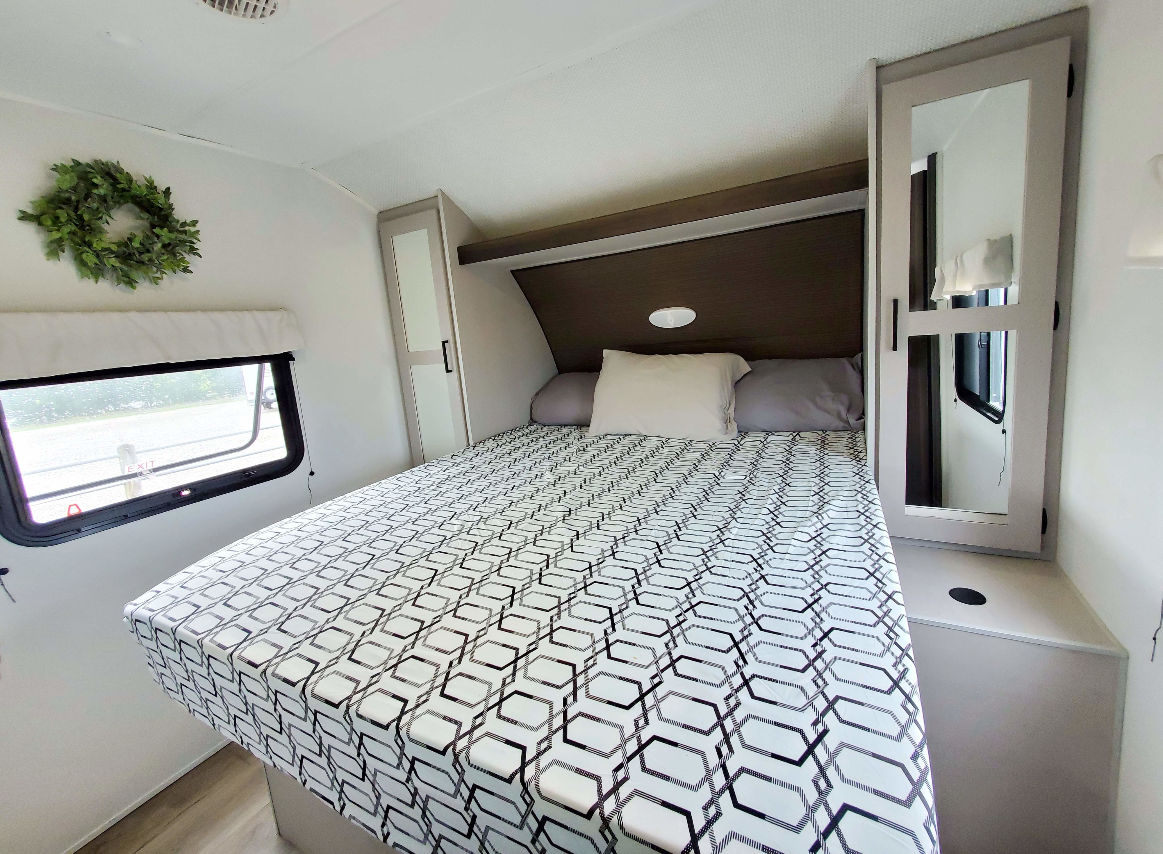 Bright rv rental bedroom features a bed with geometric bedding, mirrored cabinets, and a window for a comfortable stay.. Heartland RVs Prowler 2023