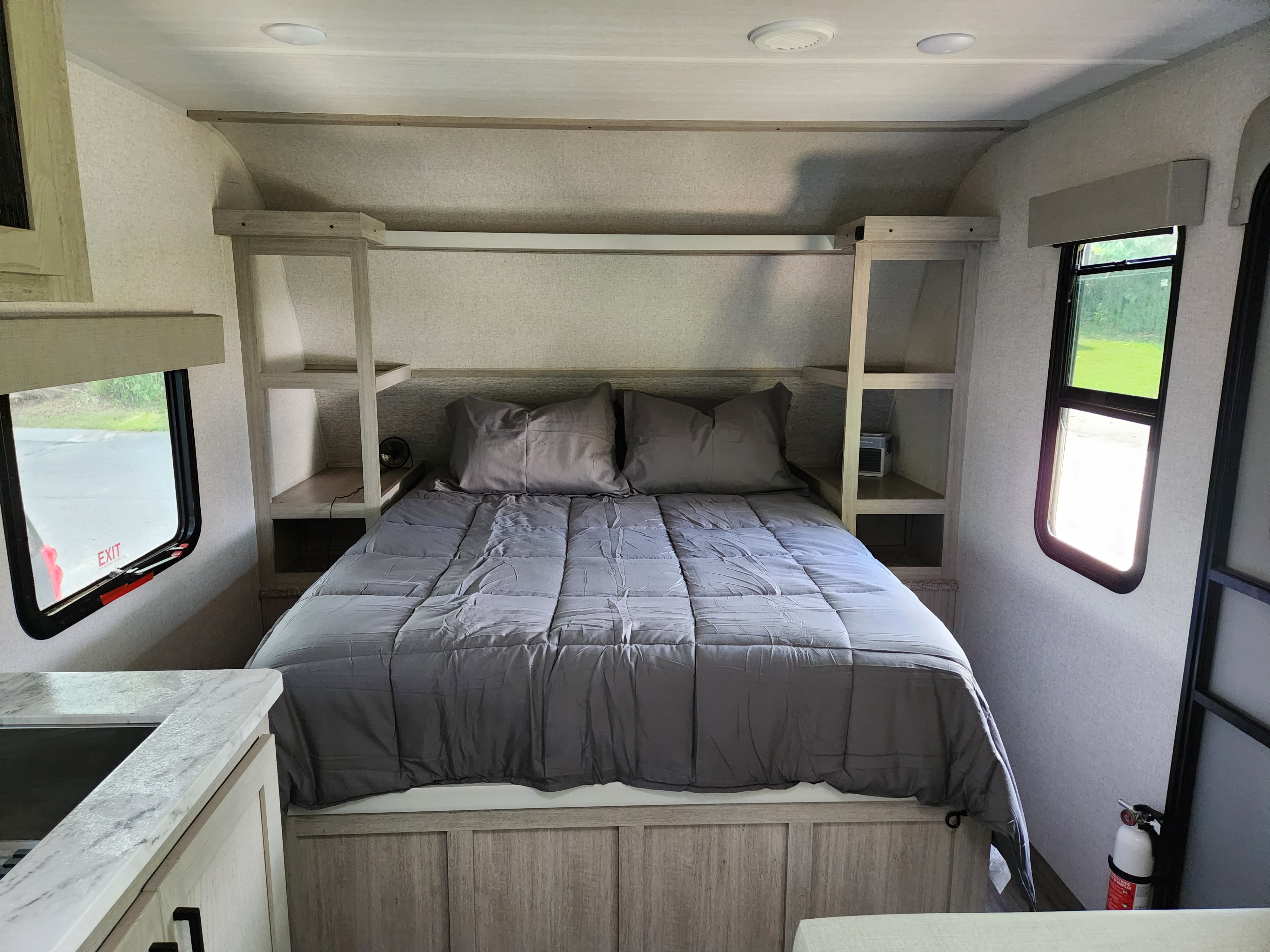 Inside a compact RV rental bedroom: queen bed, built-in storage, windows, and safety features like an extinguisher.. East to West Alta 2022