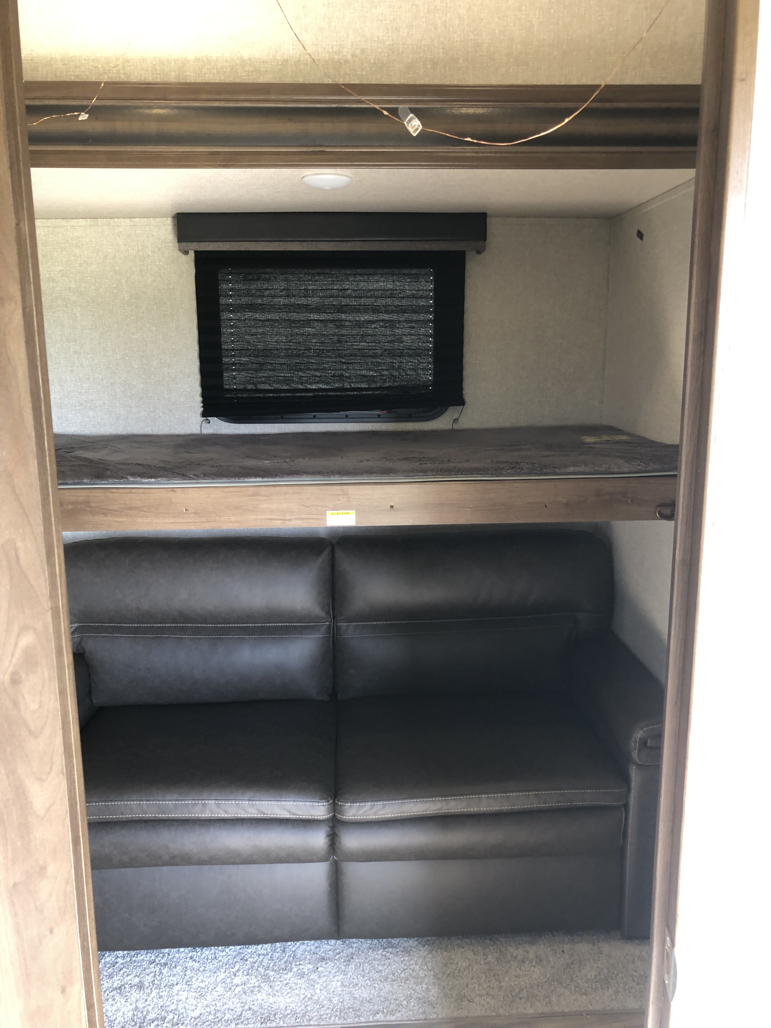 RV rental bunkhouse: A dark grey sofa is positioned under a top bunk, next to a window with a blind. Compact living space.. Keystone RV Cougar 2020