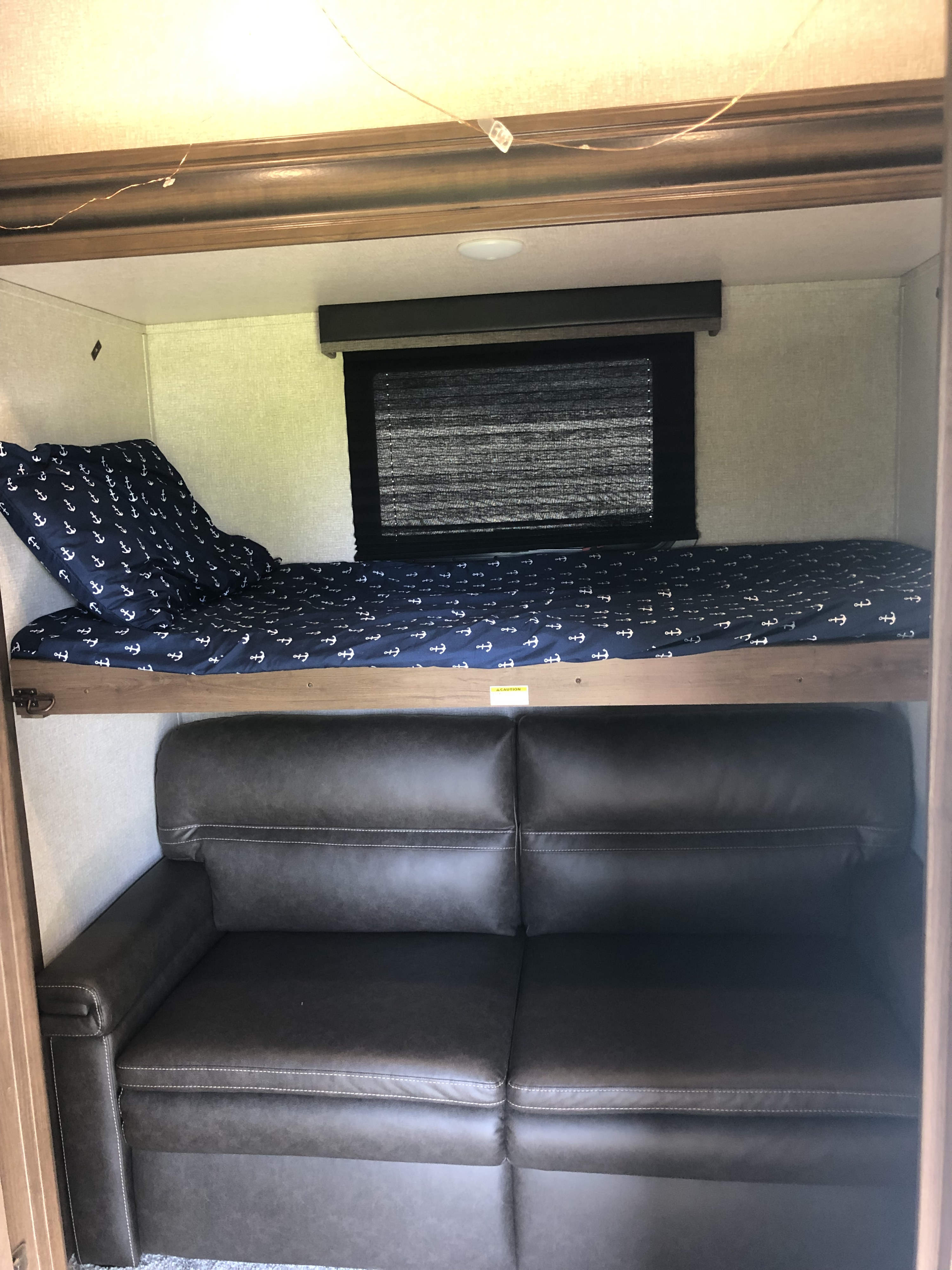 RV rental interior featuring a bunk bed with anchor bedding over a dark sofa, a cozy sleeping/lounge area.. Keystone RV Cougar 2020