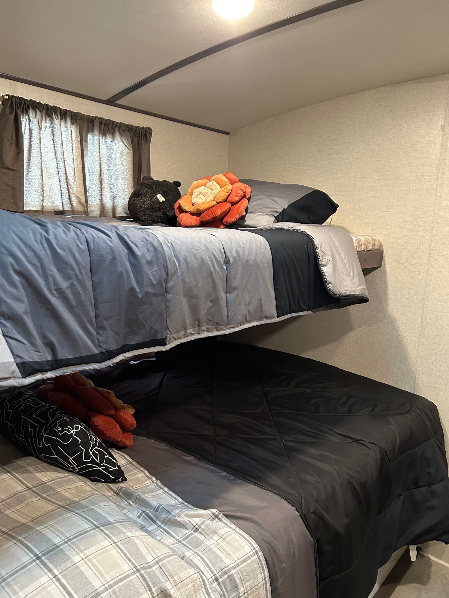 Inside an RV rental: two bunk beds with varied bedding, decorative pillows, and window curtains.. Keystone RV Sunset Trail 2018