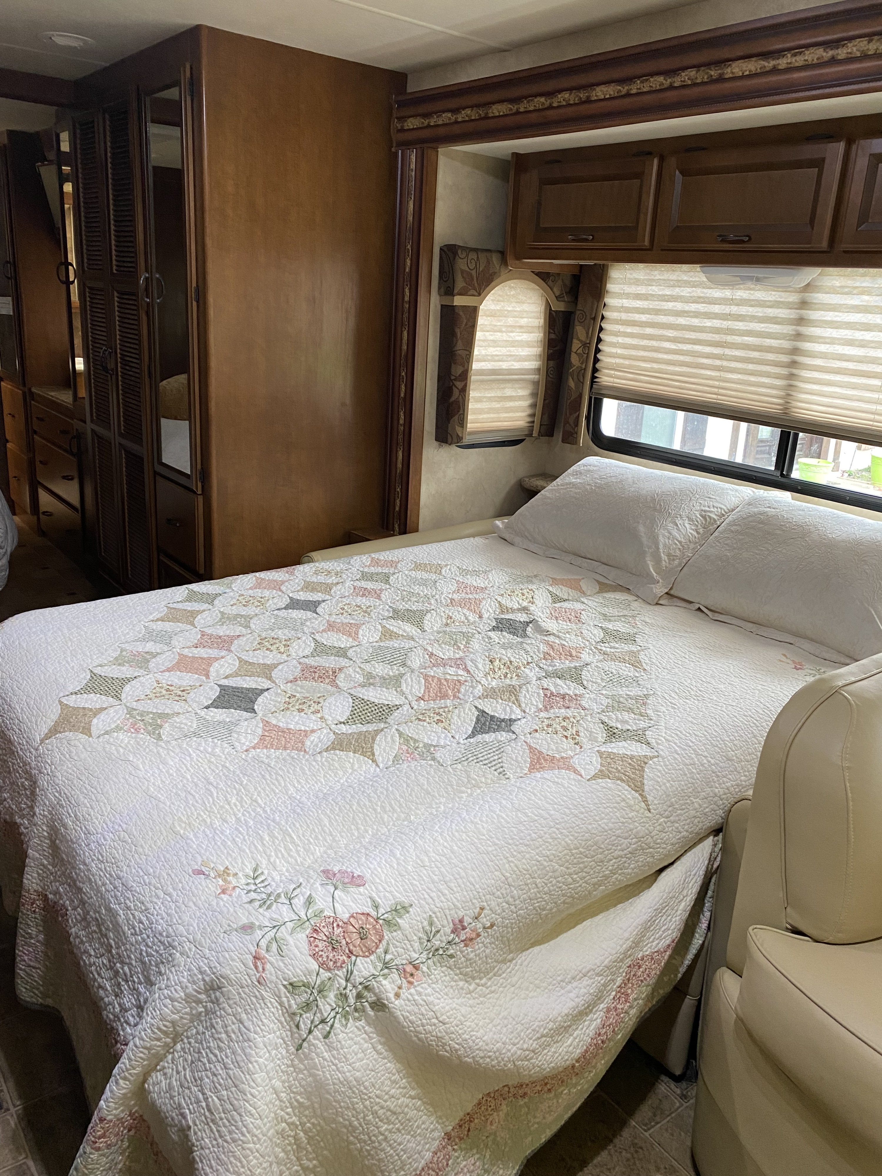 Comfortable RV rental bedroom: patterned quilt, wooden cabinets, windows with blinds, and seating for restful nights.. Thor Hurricane 2014