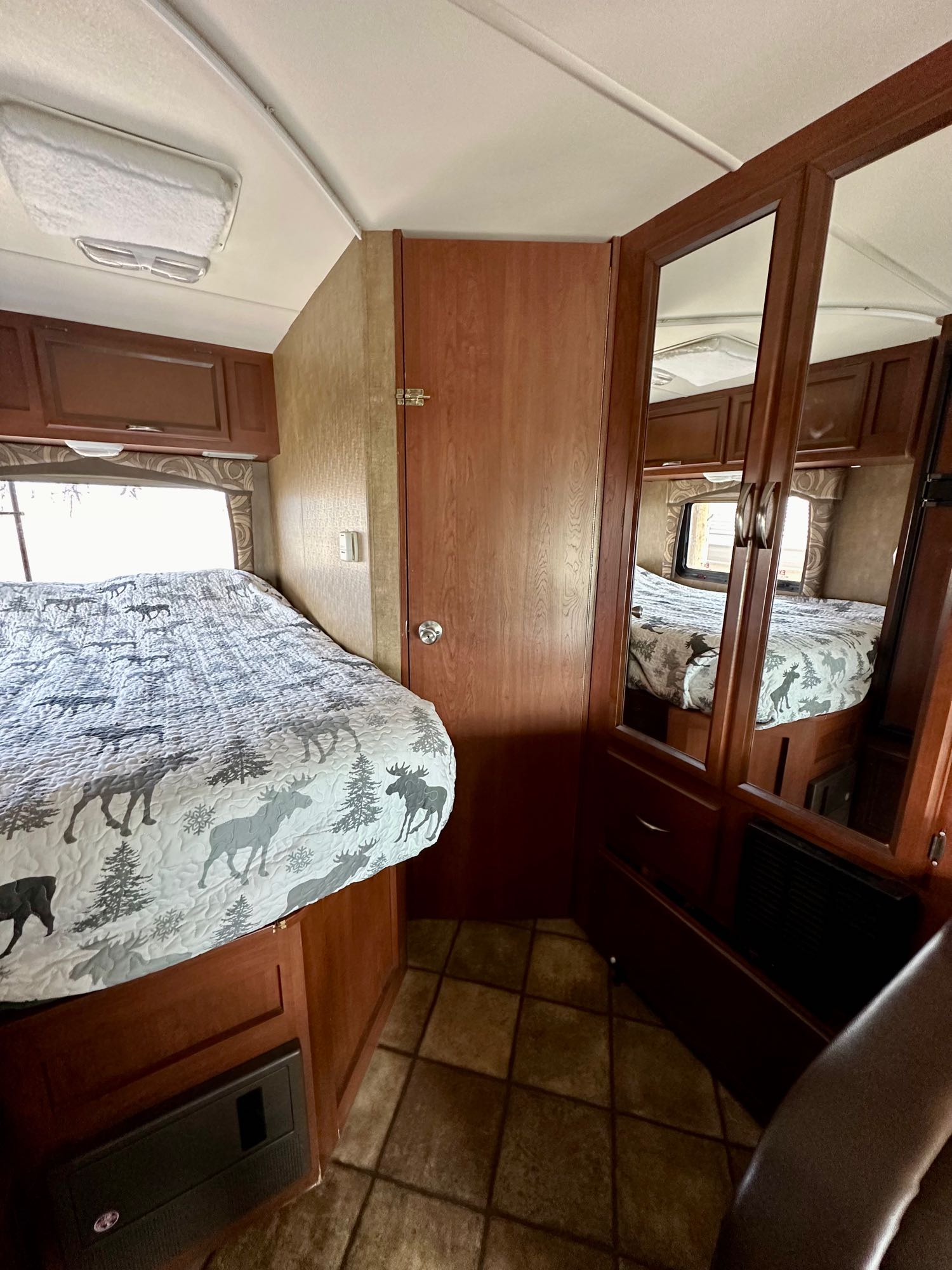 Cozy RV rental bedroom featuring a moose-themed bed, mirrored closet, and wood cabinetry. Ideal for your travel adventures.. Thor Chateau 2014