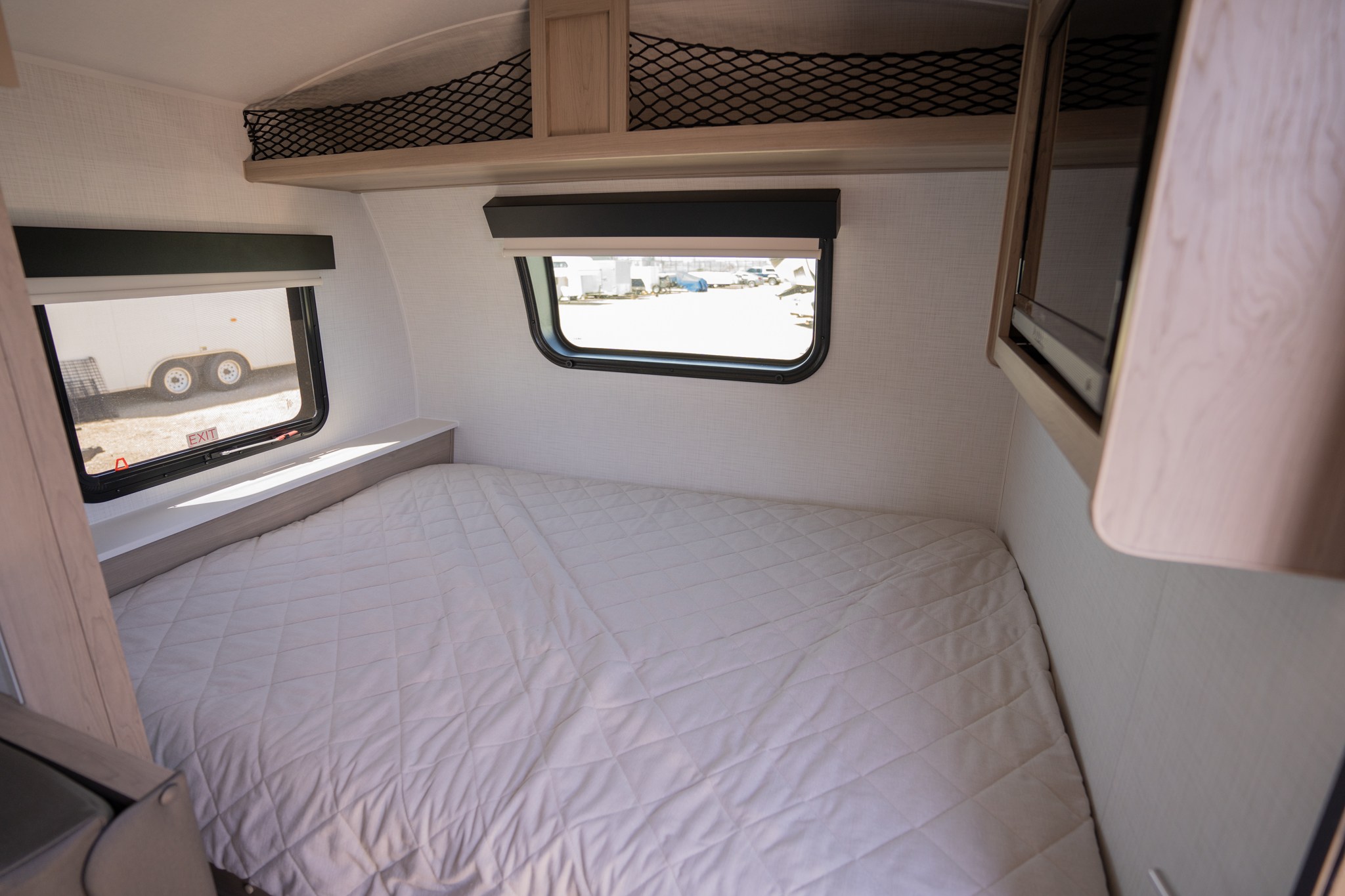 RV rental bedroom features a comfy quilted bed, dual windows with exterior views, overhead net storage, and a TV.. Forest River Flagstaff E-Pro 2024