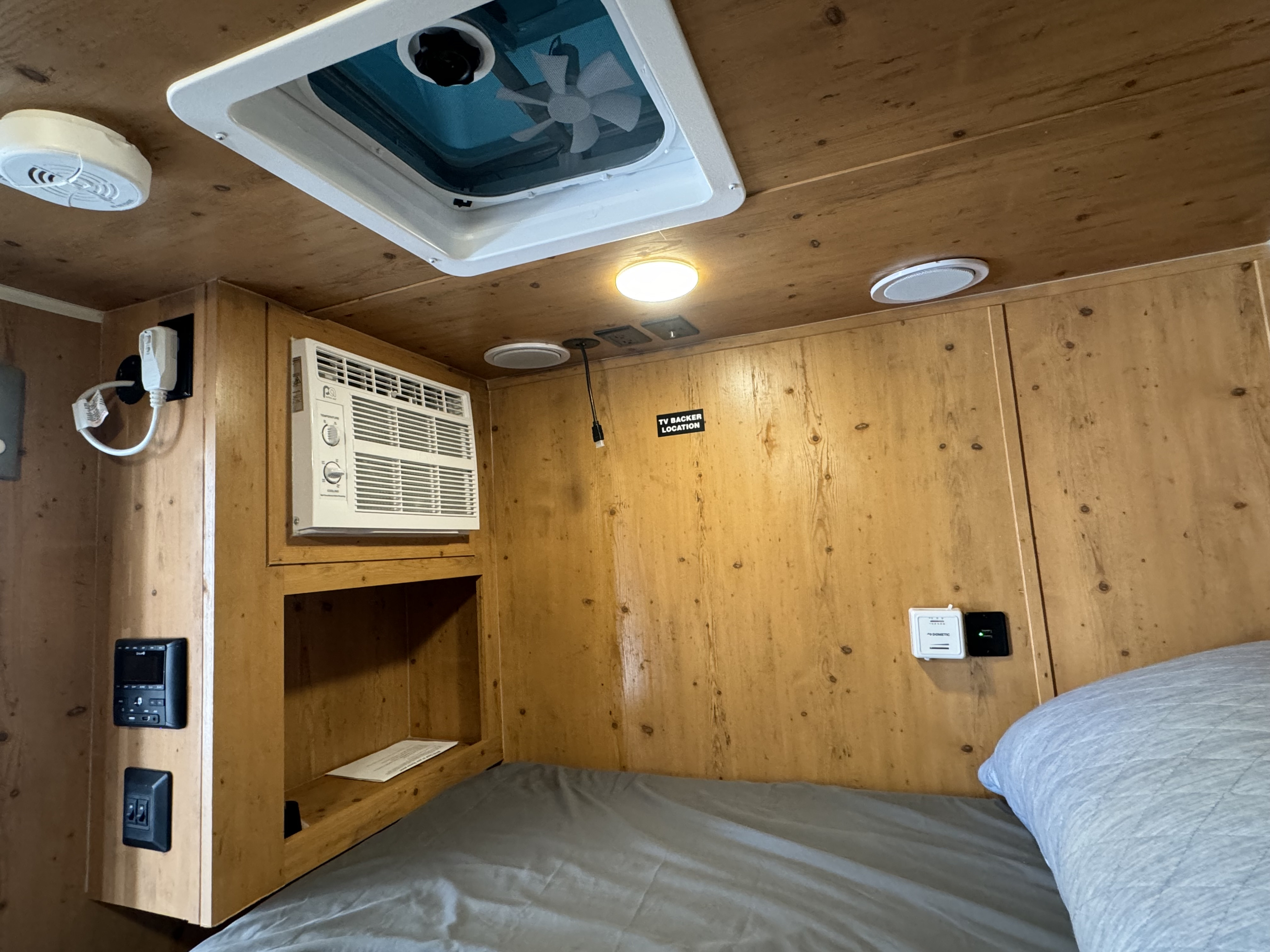 Cozy RV rental interior: wooden walls, bed, window AC, ceiling fan, and panel controls for your travel comfort.. Sunray 109E 2022