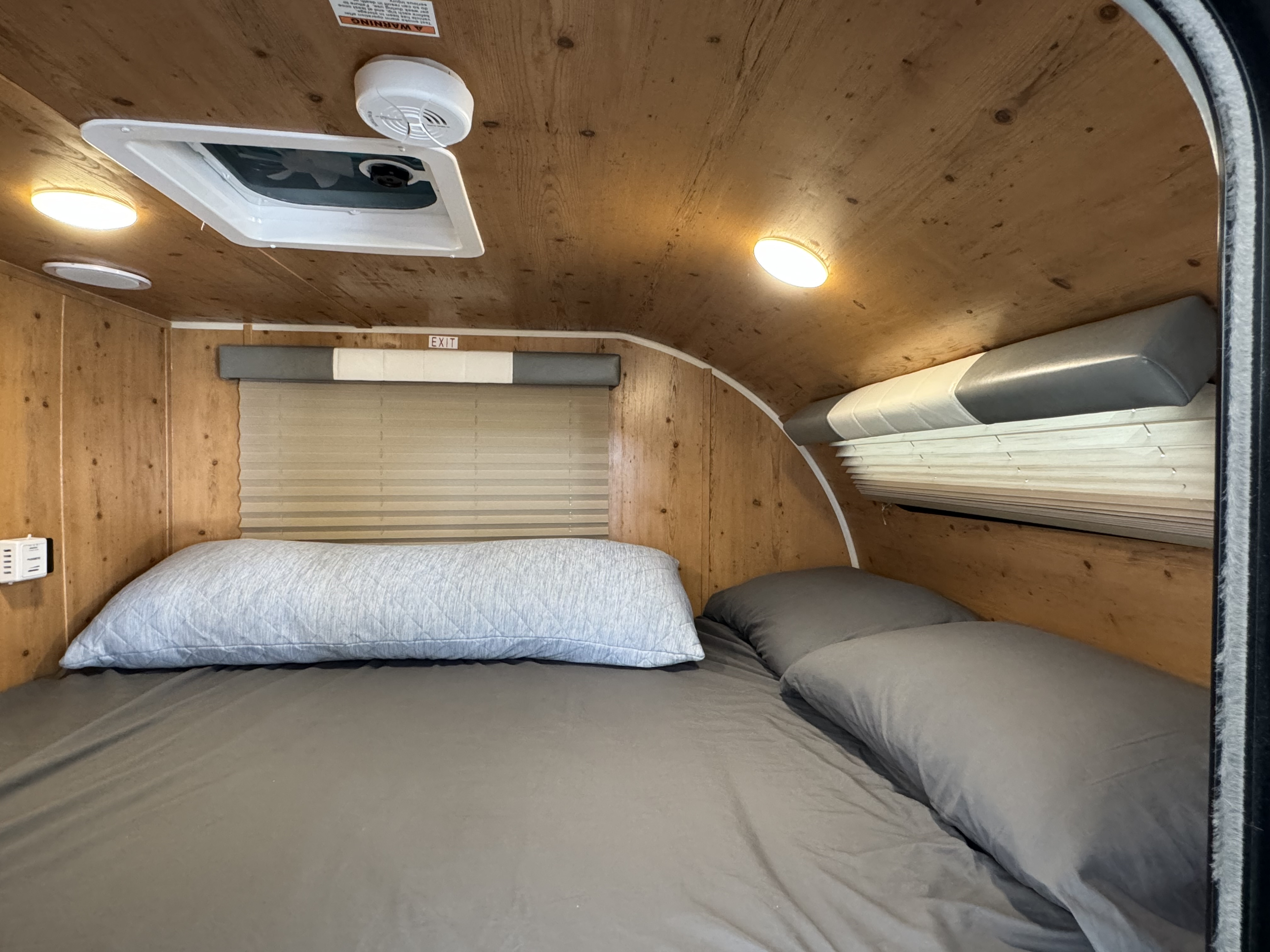 Comfortable RV rental interior showing a bed with grey bedding, wood walls, ceiling fan, and window blinds.. Sunray 109E 2022