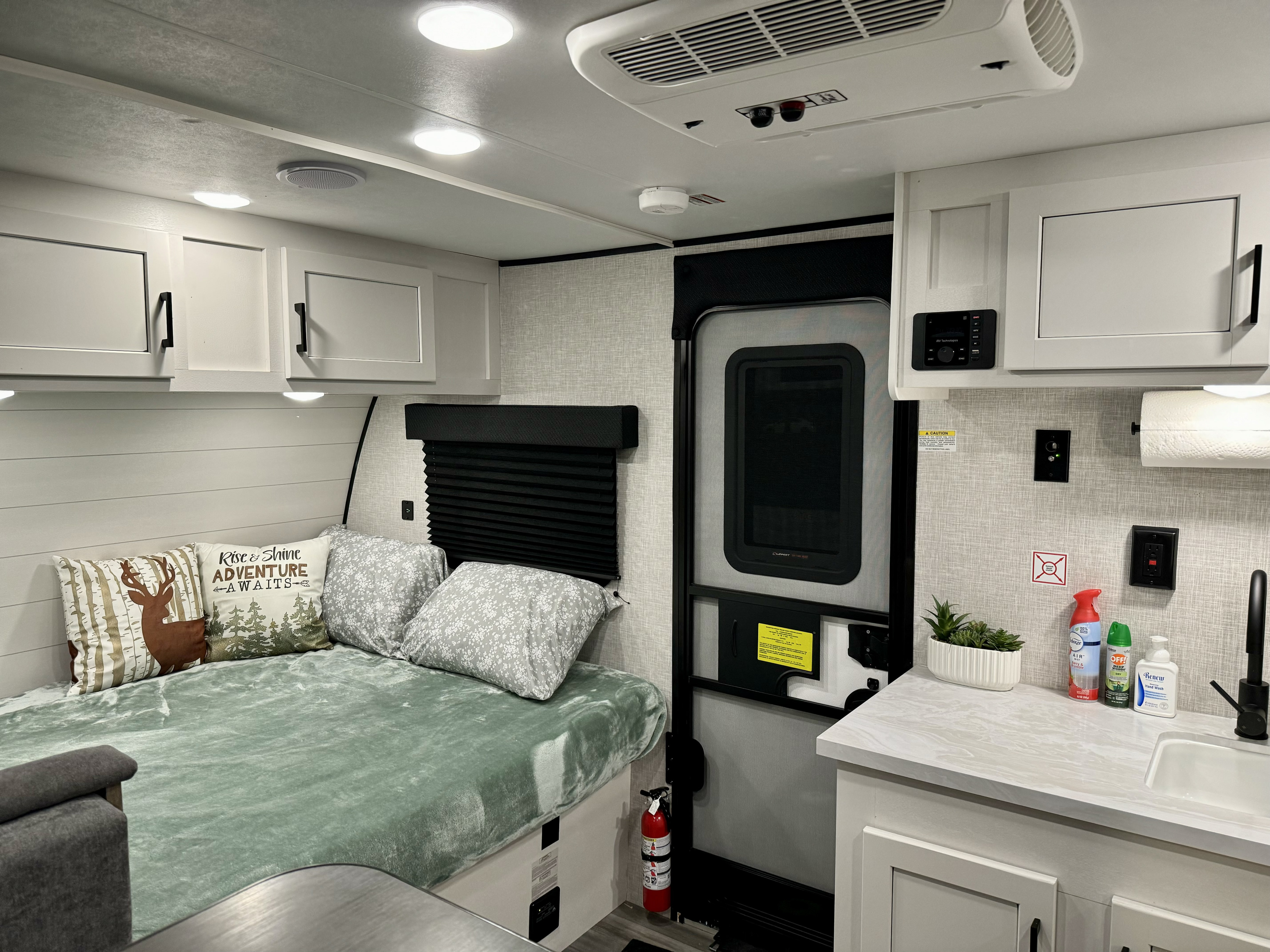 Bright RV rental interior featuring a comfy bed, compact kitchen, and practical amenities like AC and a fire extinguisher.. Jayco Jay Flight SLX 2024