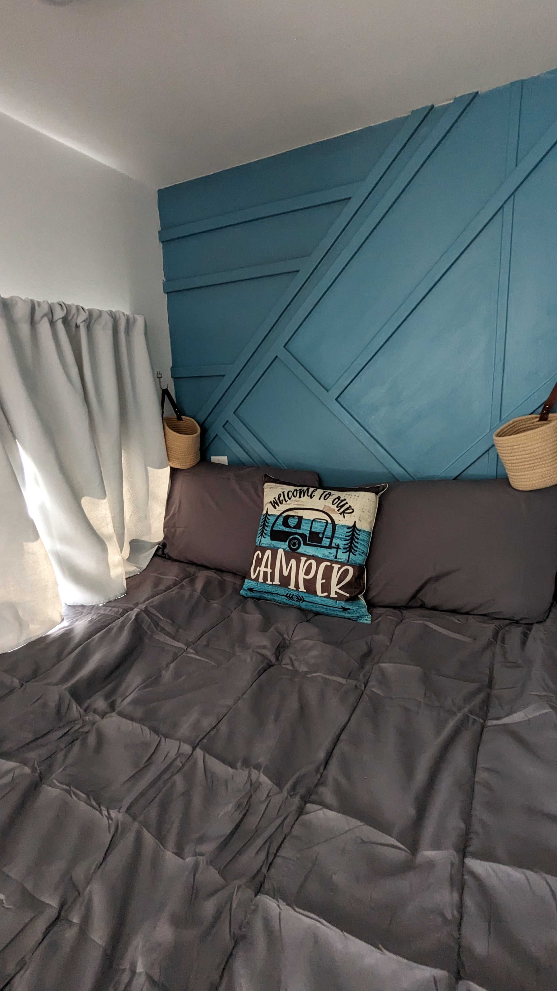 A cozy RV rental bedroom interior featuring a dark gray bed, teal geometric accent wall, and a "CAMPER" pillow.. Eclipse Milan CK 2014