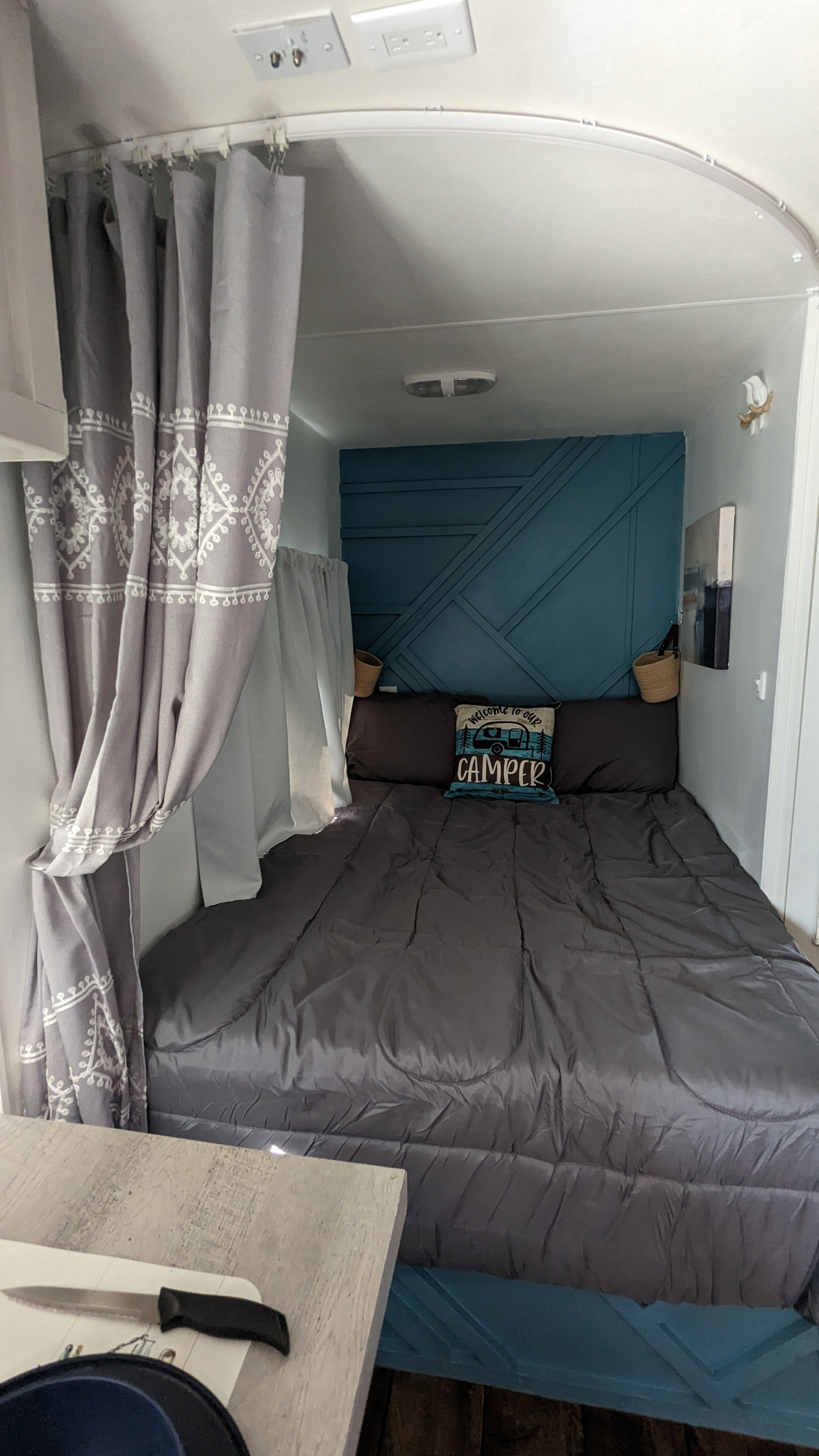 Cozy RV rental bedroom features teal paneled decor, gray bedding, and patterned privacy curtains, ideal for a camper's retreat.. Eclipse Milan CK 2014