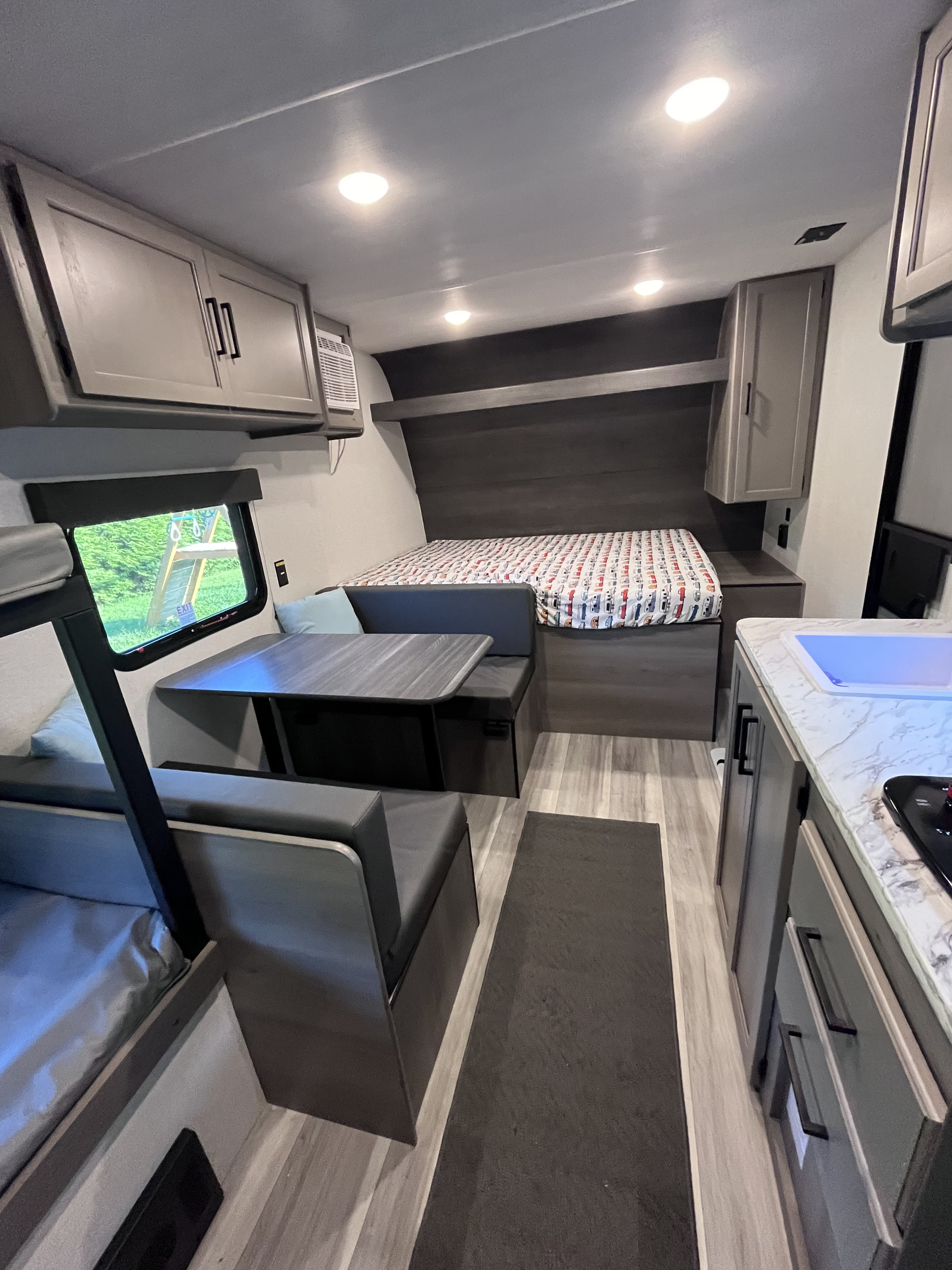 Bright RV rental interior features a cozy main bed, convertible dinette, bunk beds, and compact kitchenette.. Keystone RV Hideout Sport 2024