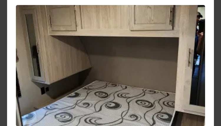 RV rental: Compact bedroom interior featuring a patterned mattress, overhead cabinets, and a mirrored wardrobe.. Coachmen Catalina Legacy 323BHDSCK 2022