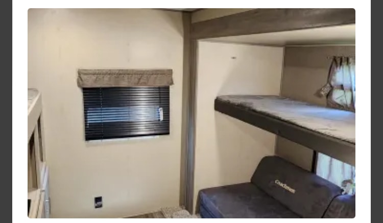 RV rental camper interior showing bunk beds, a convertible sofa, and a window with closed blinds.. Coachmen Catalina Legacy 323BHDSCK 2022