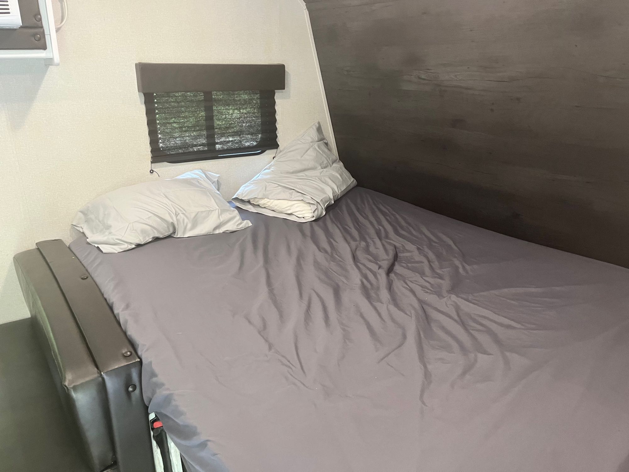 Inside an RV rental: A comfortable bed with gray linens, pillows, and a window with blinds, ready for travel.. Keystone RV Hideout 2021