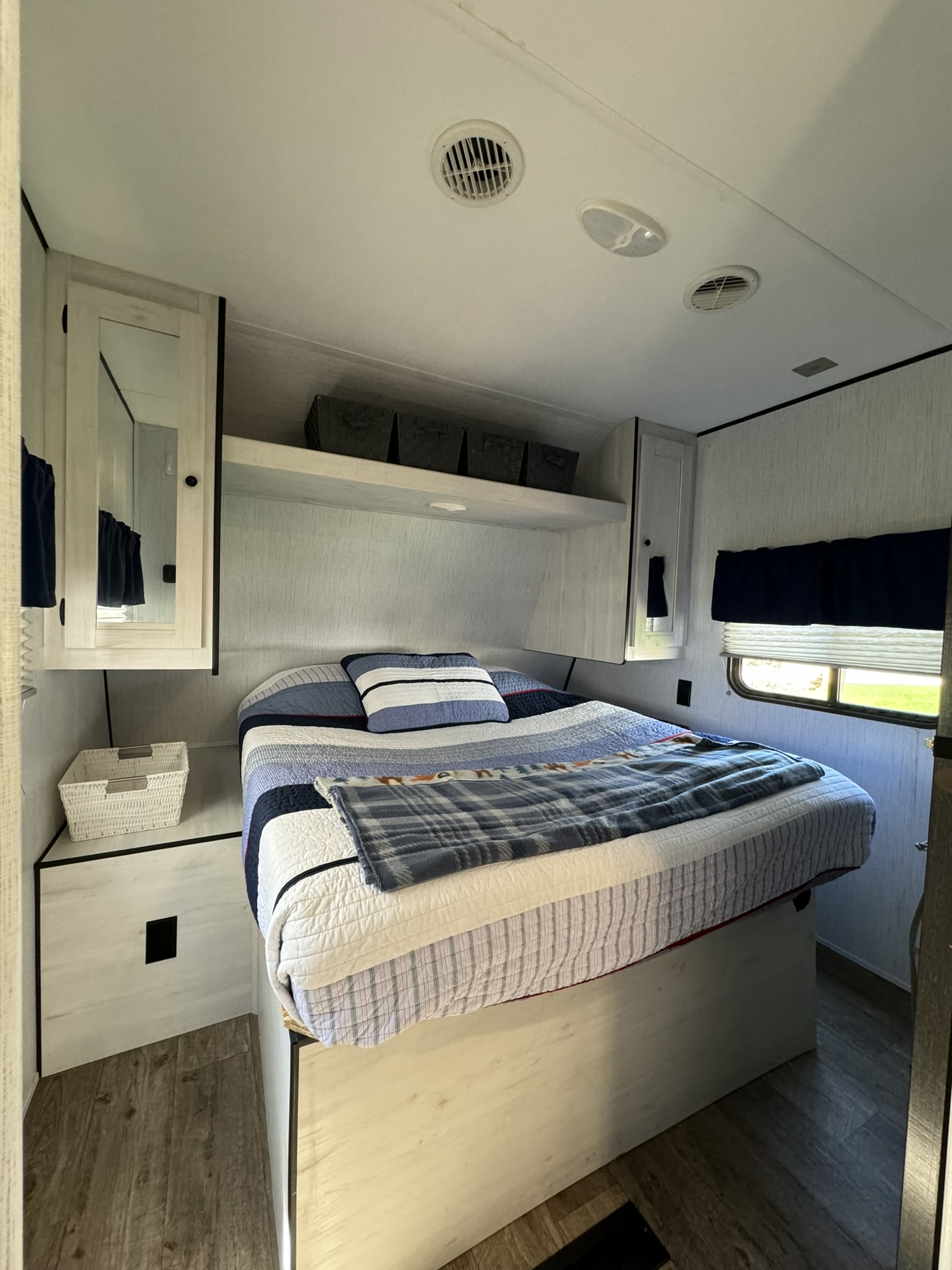RV rental bedroom: a comfy interior with blue striped bedding, overhead storage, and a window.. Heartland RVs Trail Runner 2021