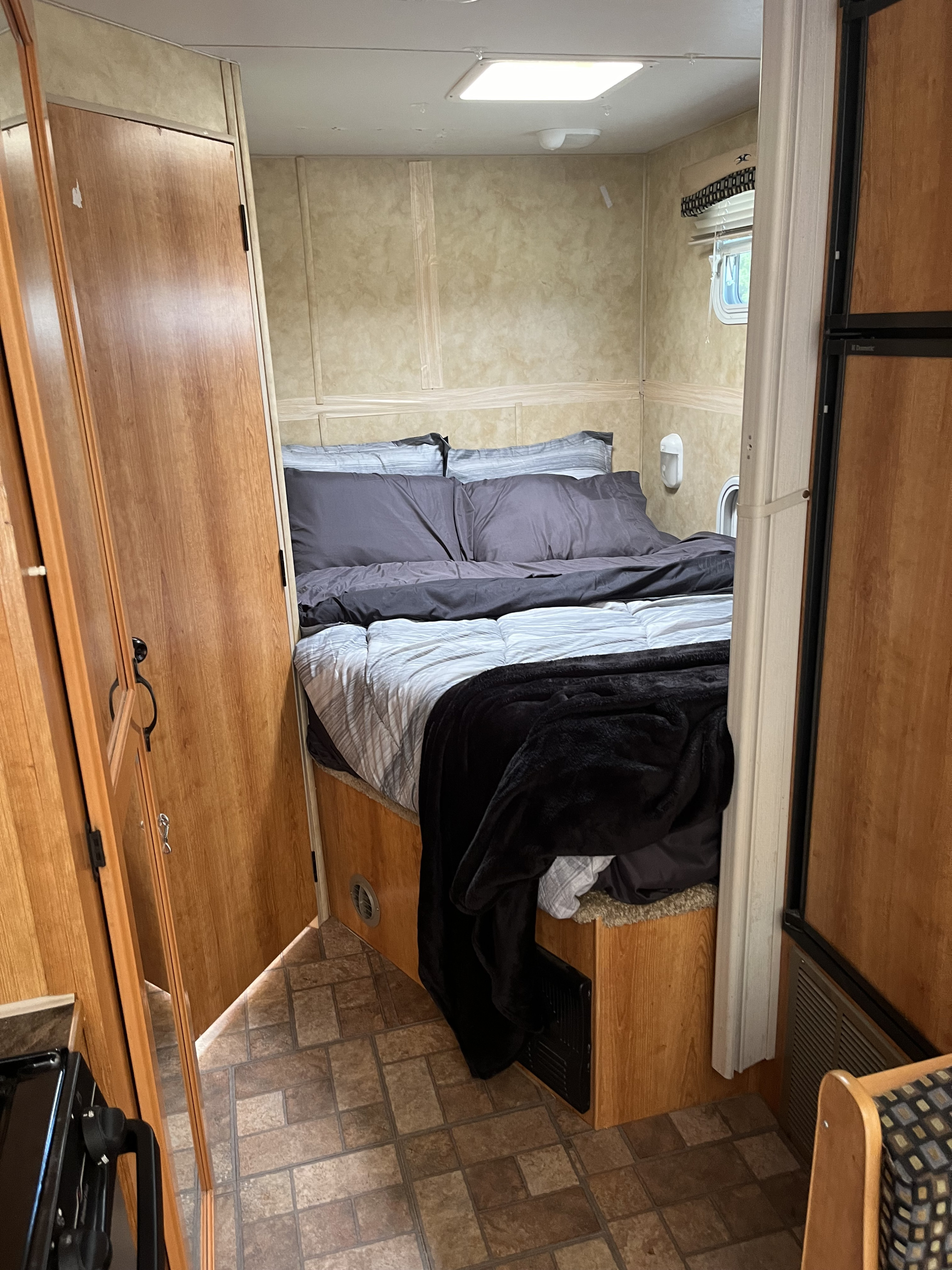 RV rental interior: a comfy bedroom with gray bedding, wooden cabinetry, and tiled flooring.. Coachmen SportsMaster 2008