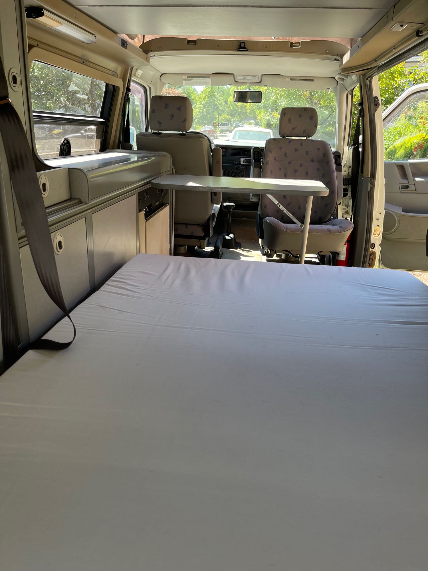 RV rental camper van interior featuring a large mattress bed, built-in kitchenette, and front swivel seats with a table.. Winnebago Eurovan Camper Eurovan Camper 2001