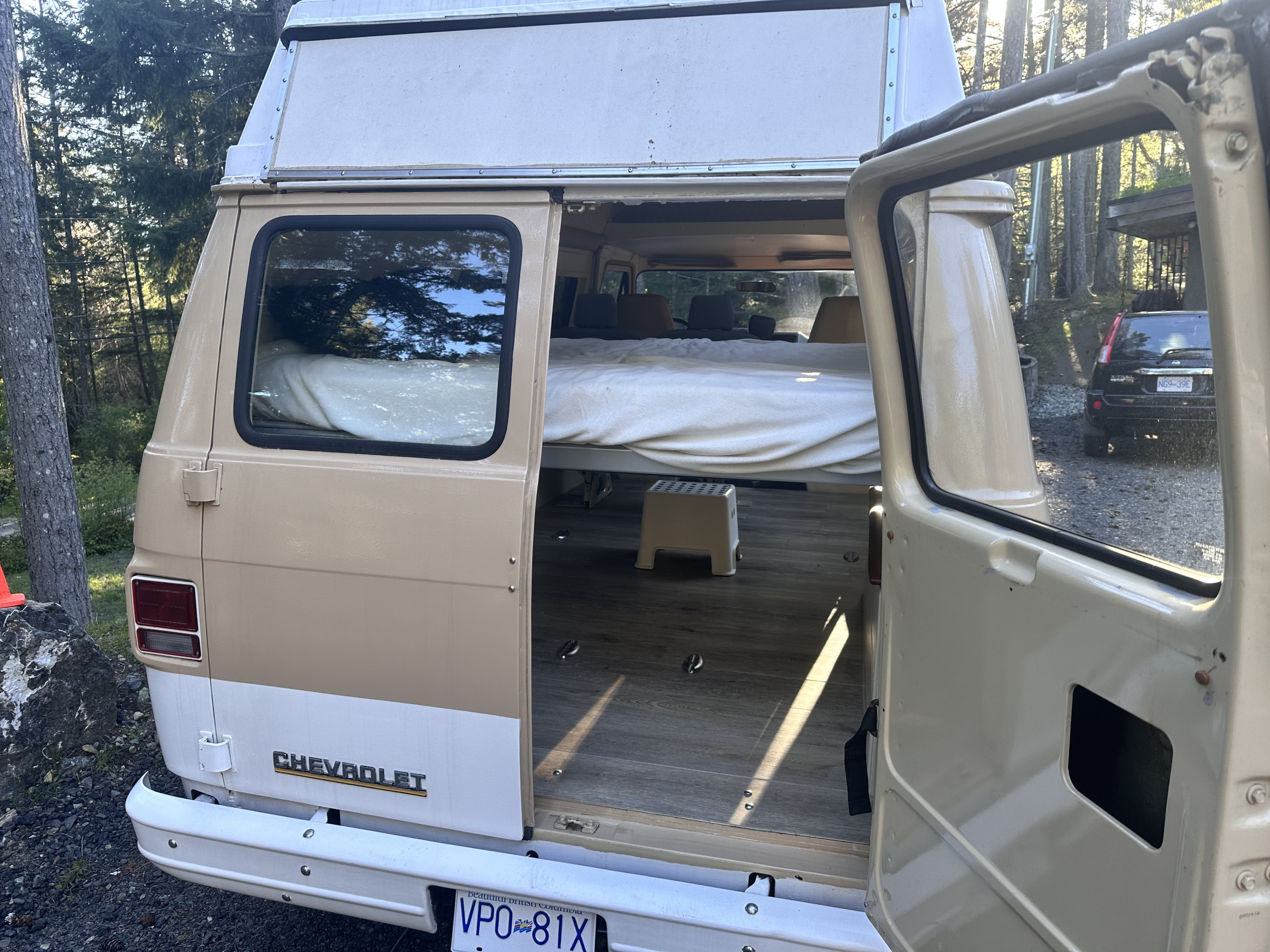 Rear view of a spacious, converted Chevrolet RV van with open doors showing a bed and wood floor, ideal for rv rental adventures.. Chevrolet G10 High Top Van 1984
