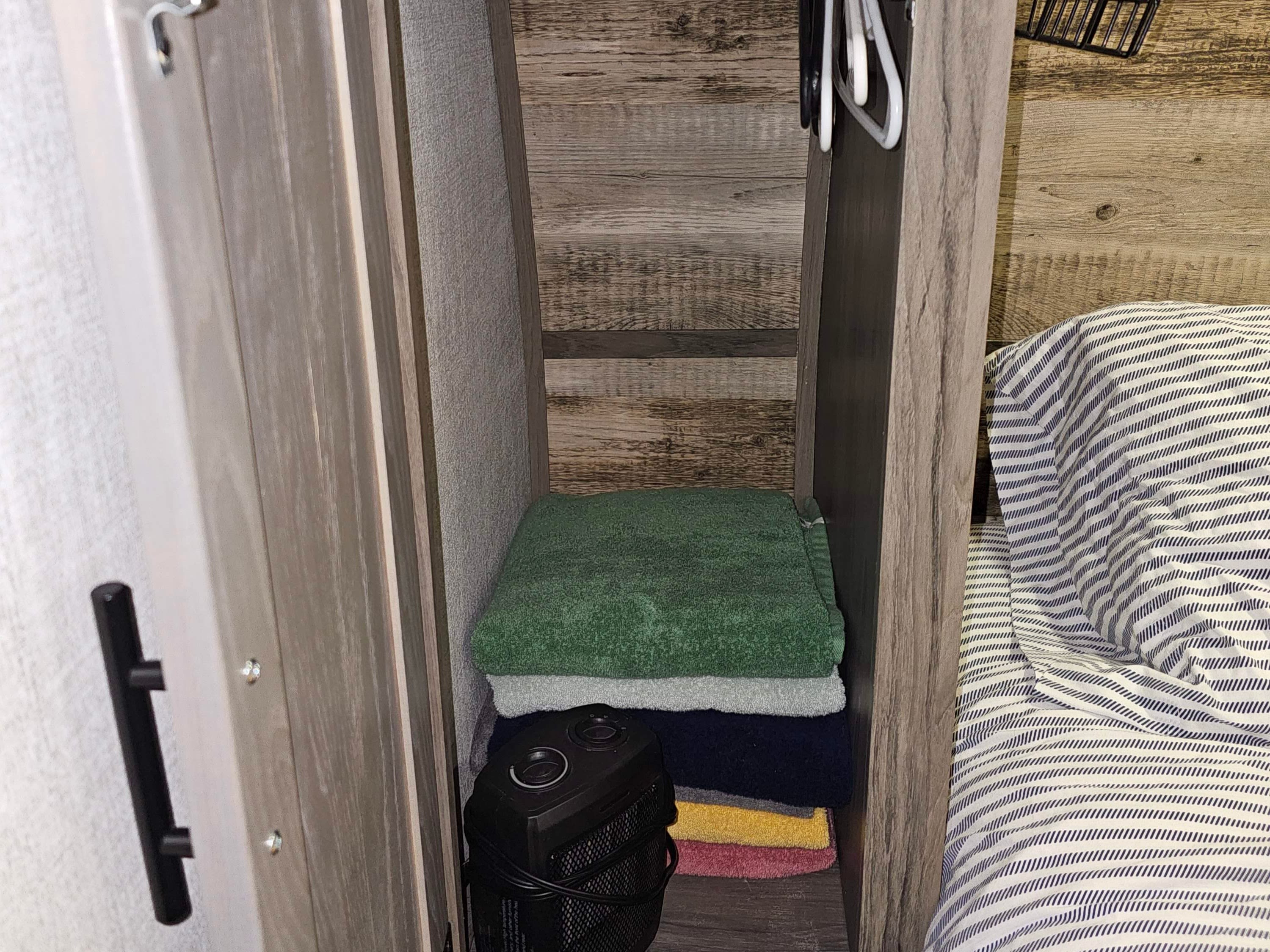RV rental bedroom closet: stacked towels, a heater, and hangers in compact storage next to the striped bed.. Gulf Stream Ameri-Lite 2022