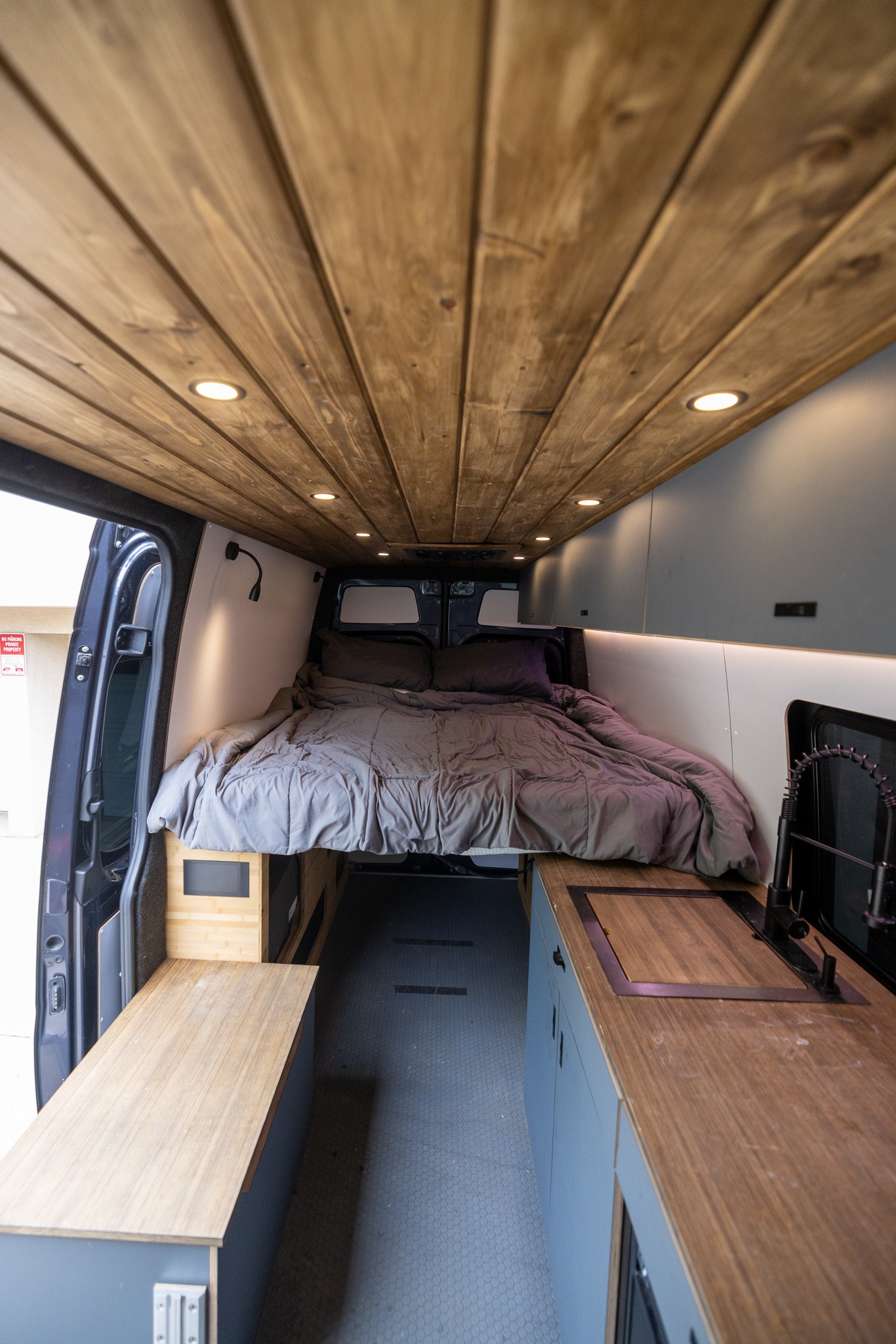 Modern rv rental interior with wood plank ceiling, cozy bed, & kitchen setup. Perfect for camper van travel.. Mercedes Sprinter 2500 2024