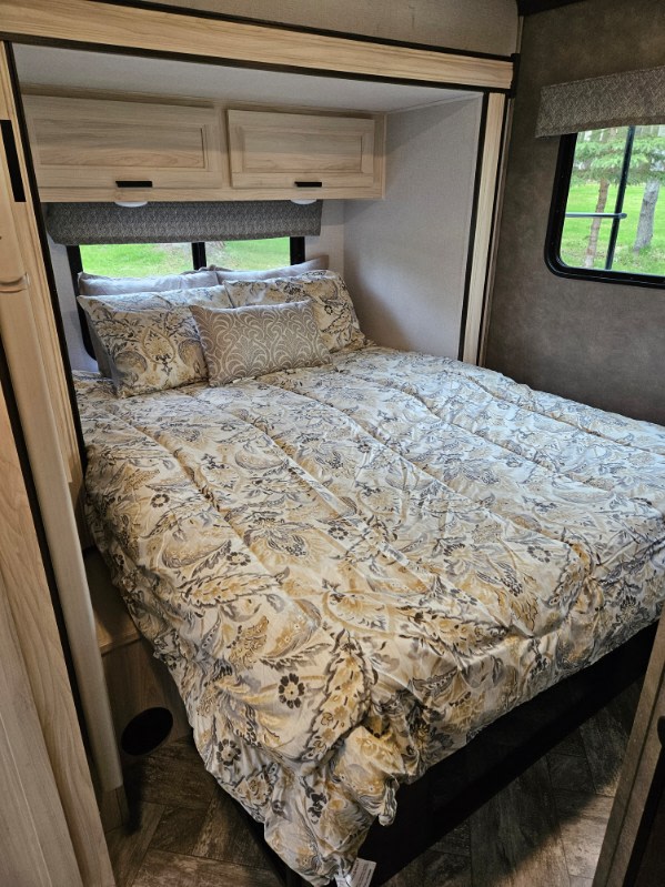 Cozy RV rental bedroom featuring a comfortable bed with patterned bedding, overhead cabinets, and a window view of nature.. Forester LE 2022