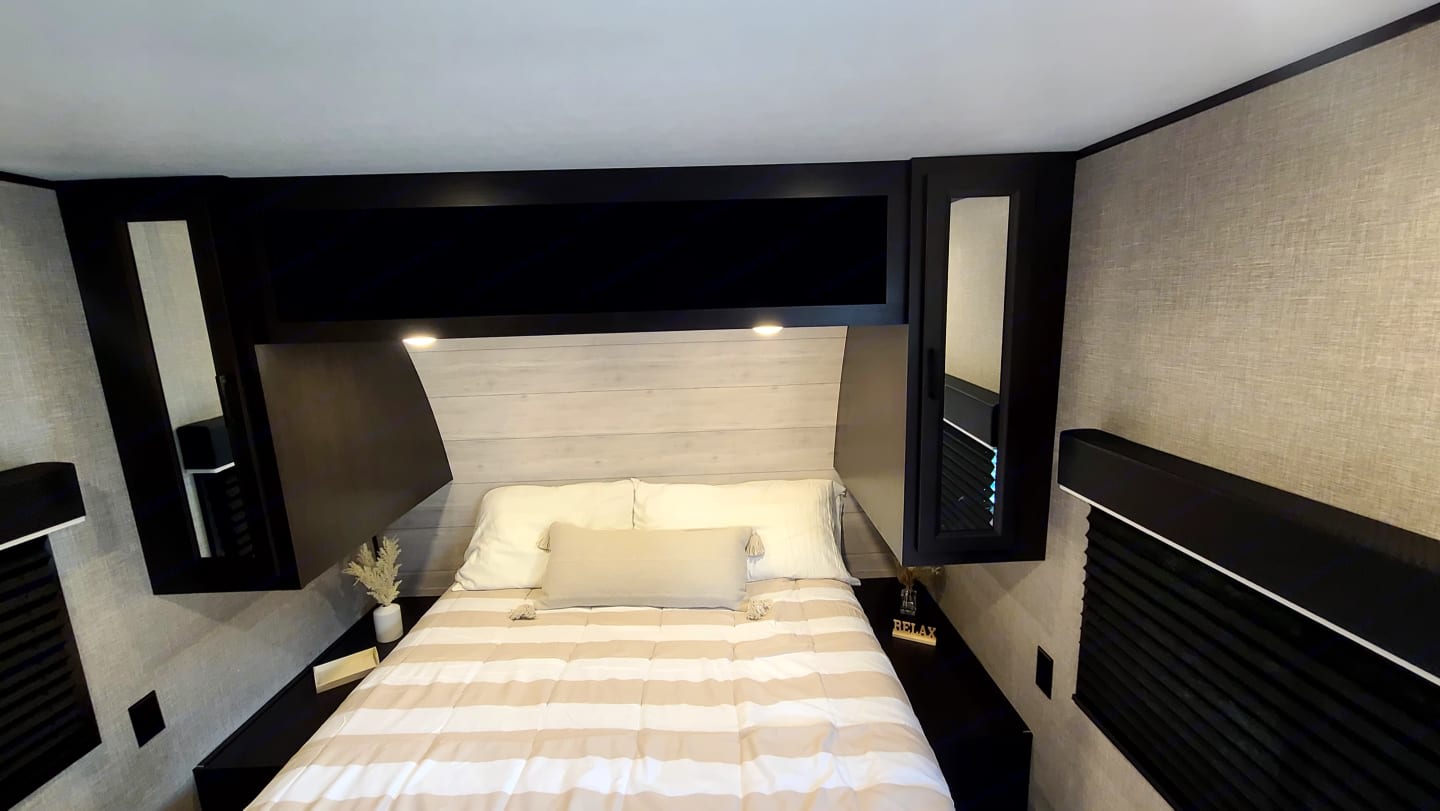Cozy RV rental bedroom with striped bedding, overhead storage, and mirrored cabinets. Ideal for travel comfort.. Jayco Jay Flight 2023