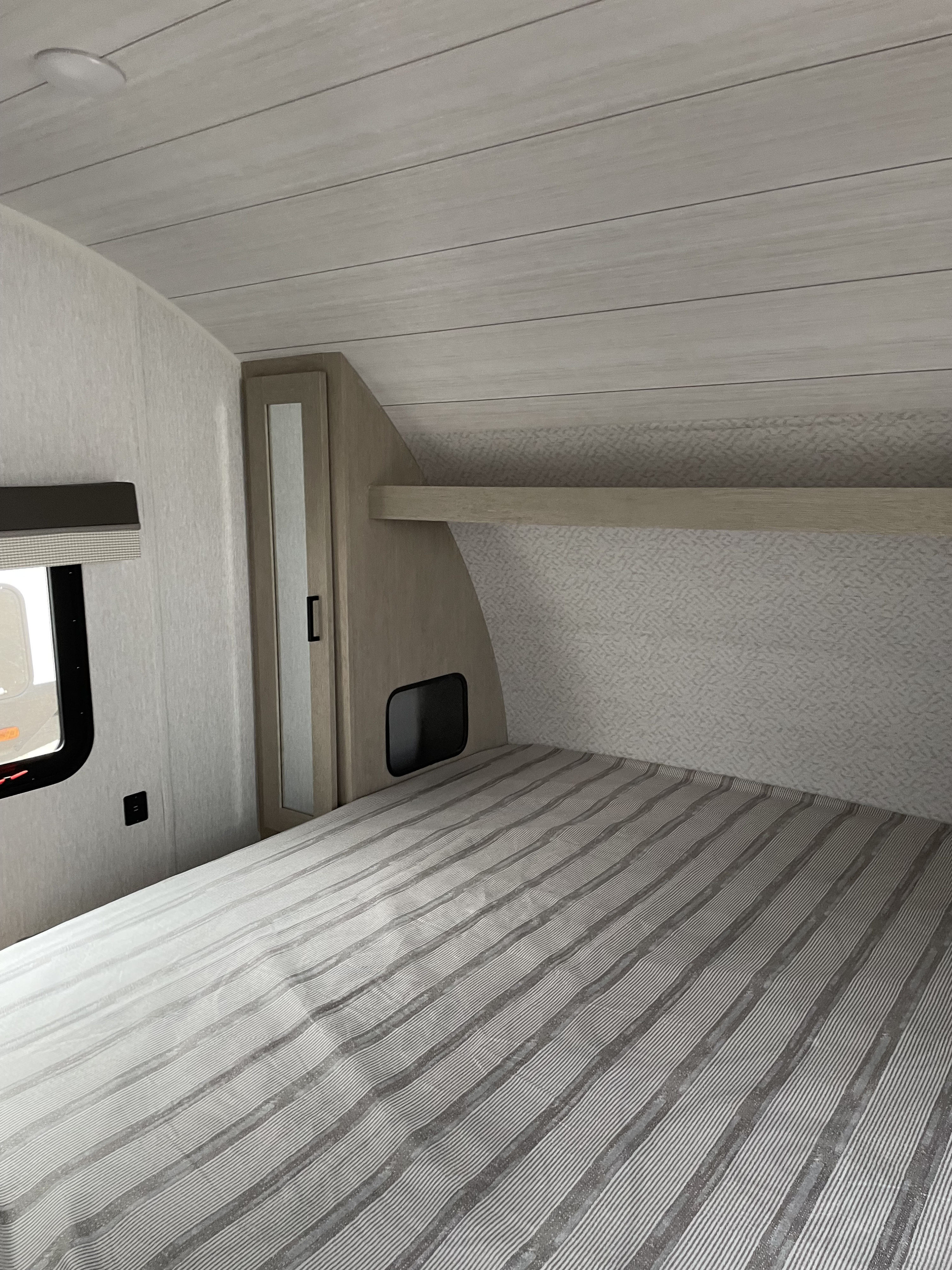 Step inside this modern RV rental bedroom featuring striped bedding, built-in storage, and a light planked ceiling.. Salem 240BHXLX 2023