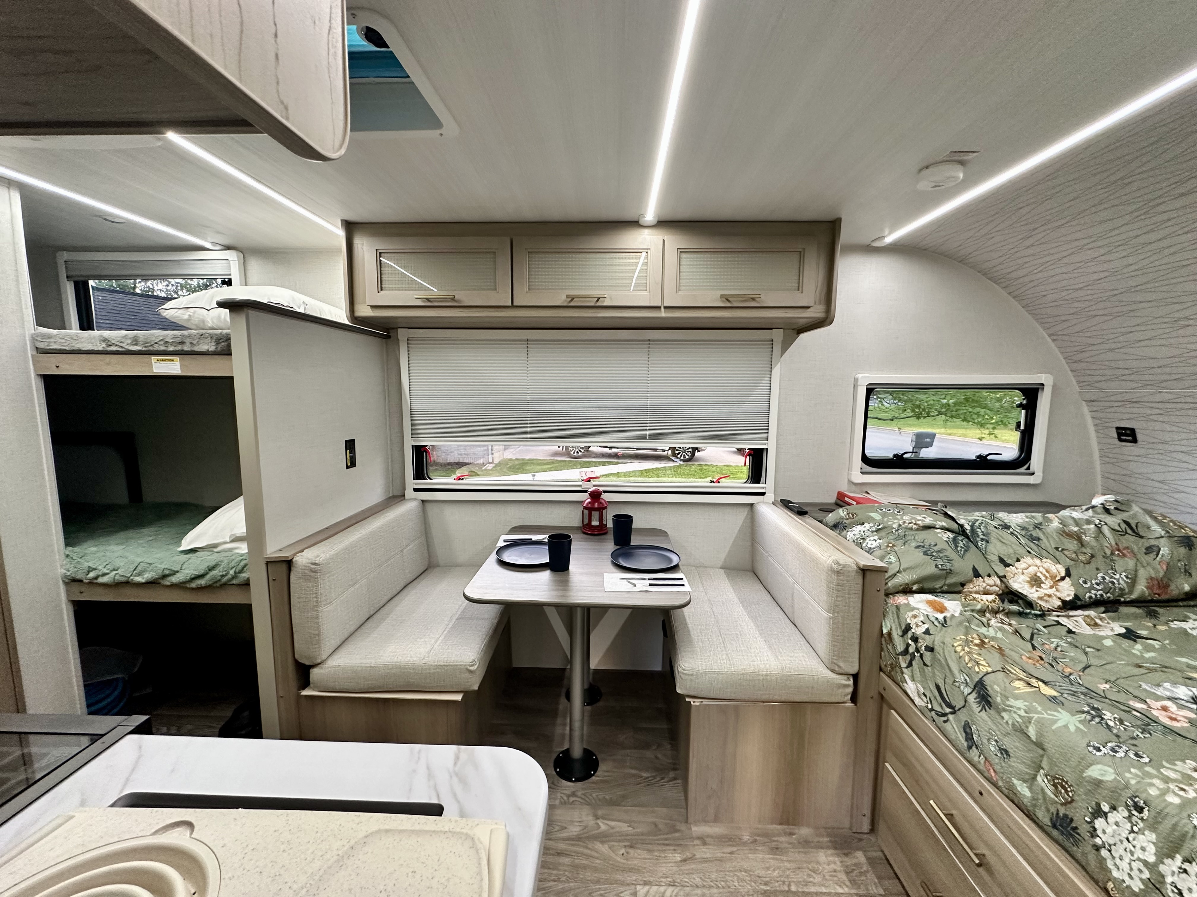 Inside an RV rental: bunk beds, a dinette, and a main bed with floral bedding offer cozy, compact living.. Keystone RV OBX 17BH 2024